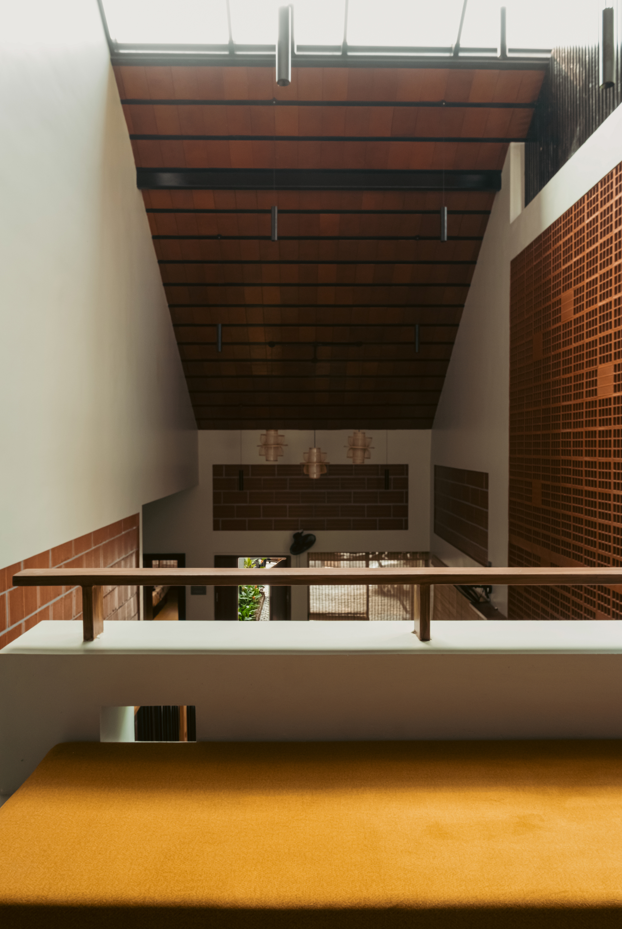 View up a stairwell void to a terracotta-lined sloped ceiling and skylight, with a perforated brick wall on the right