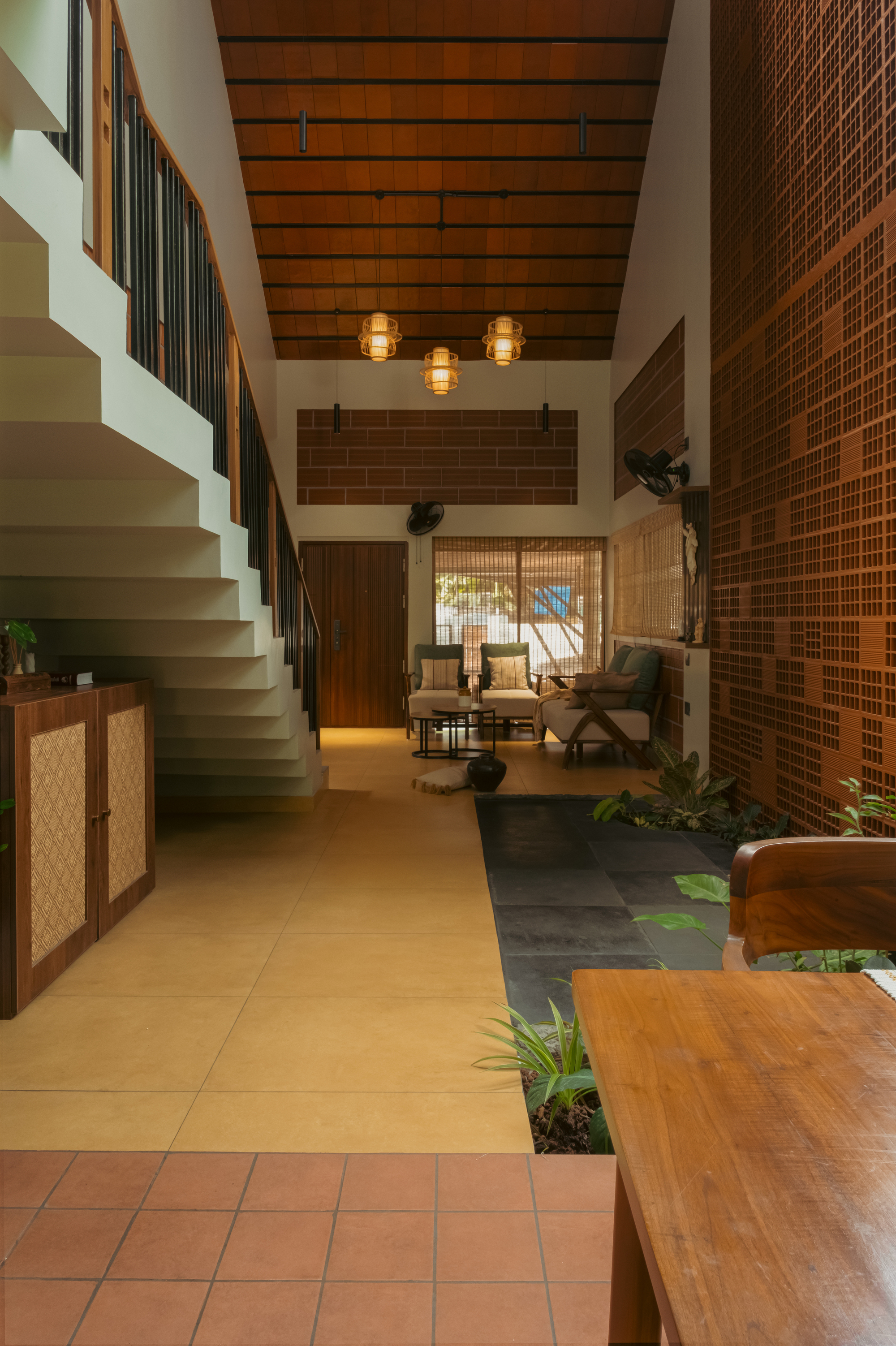 Long view down the hall past a staircase and cabinet to a seating area, with pendant lamps under a pitched timber ceiling