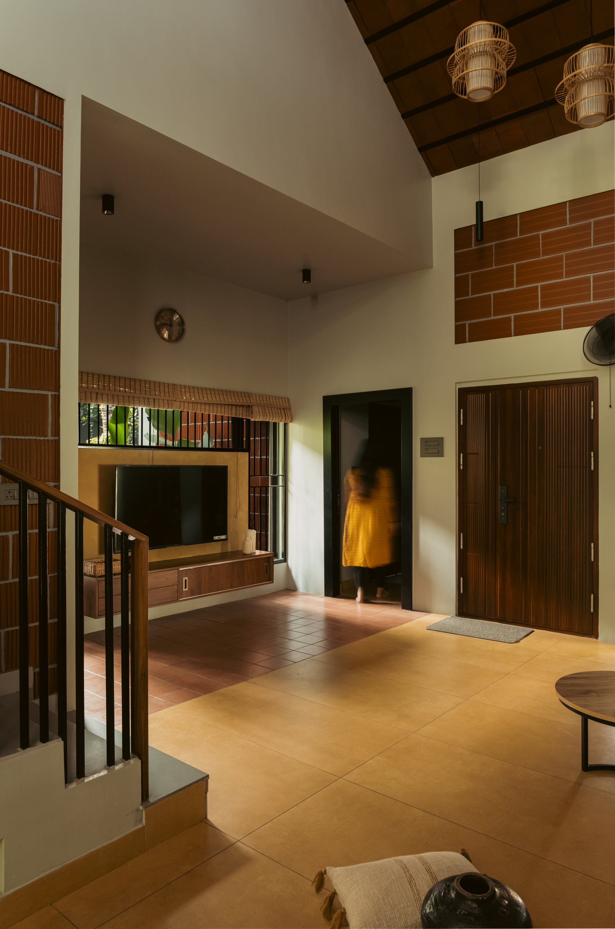 Double-height living space with exposed brick panels, a pitched timber ceiling and a blurred figure in a yellow dress crossing the doorway