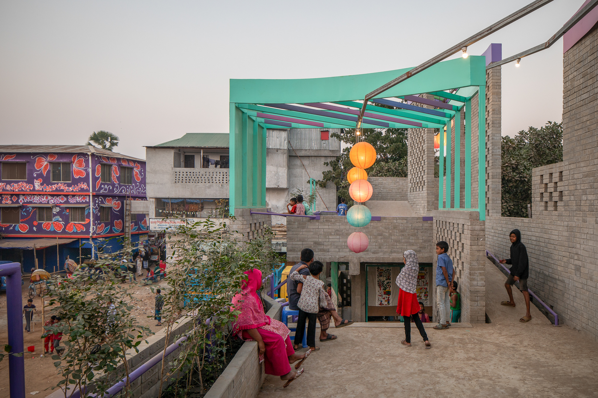 Rooftop terrace with a teal pergola, hanging paper lanterns and perforated brick walls, children gathered at dusk