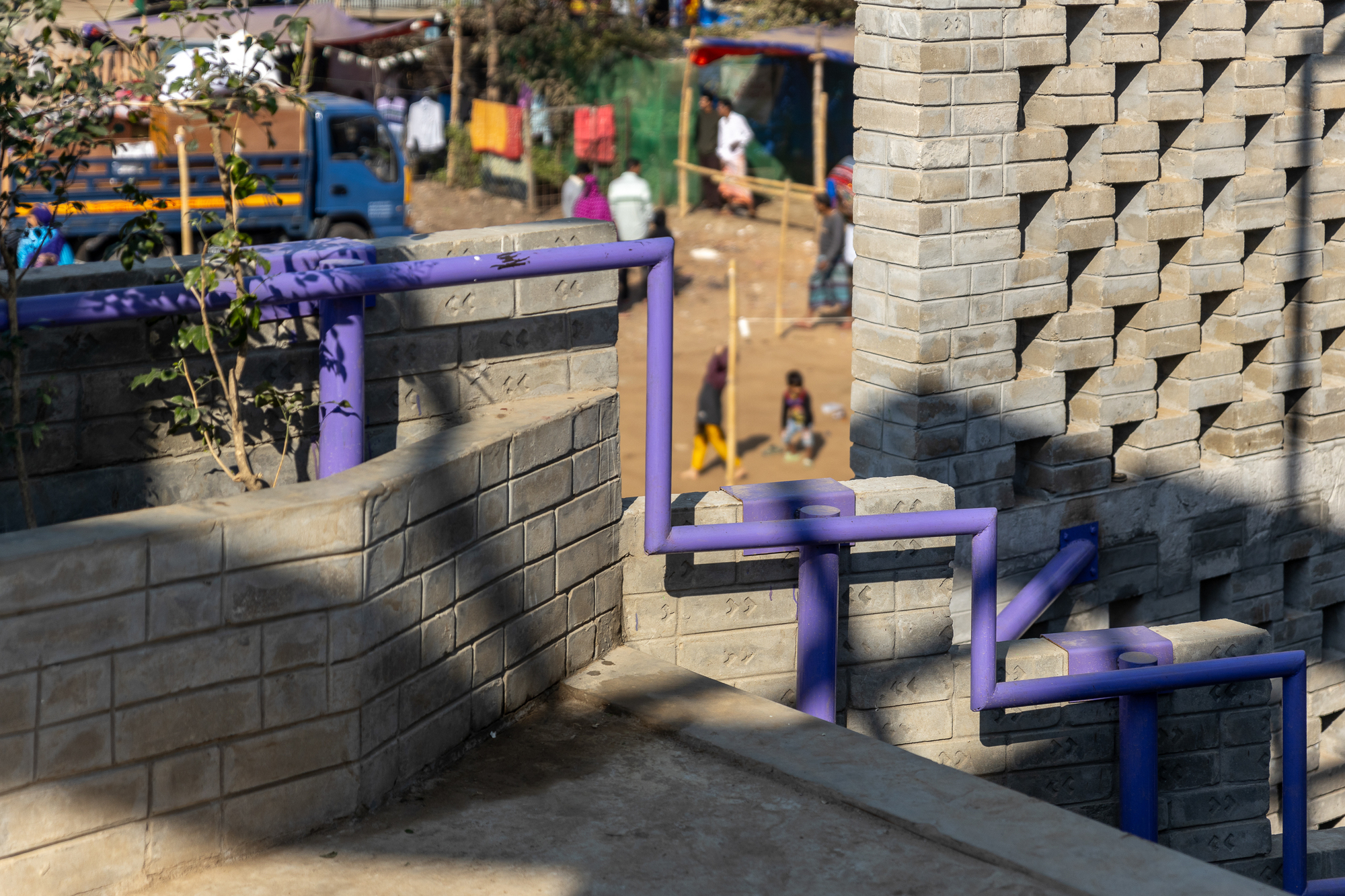 Purple steel railing zigzagging along low brick walls, with a perforated brick screen and a busy street below in afternoon sun
