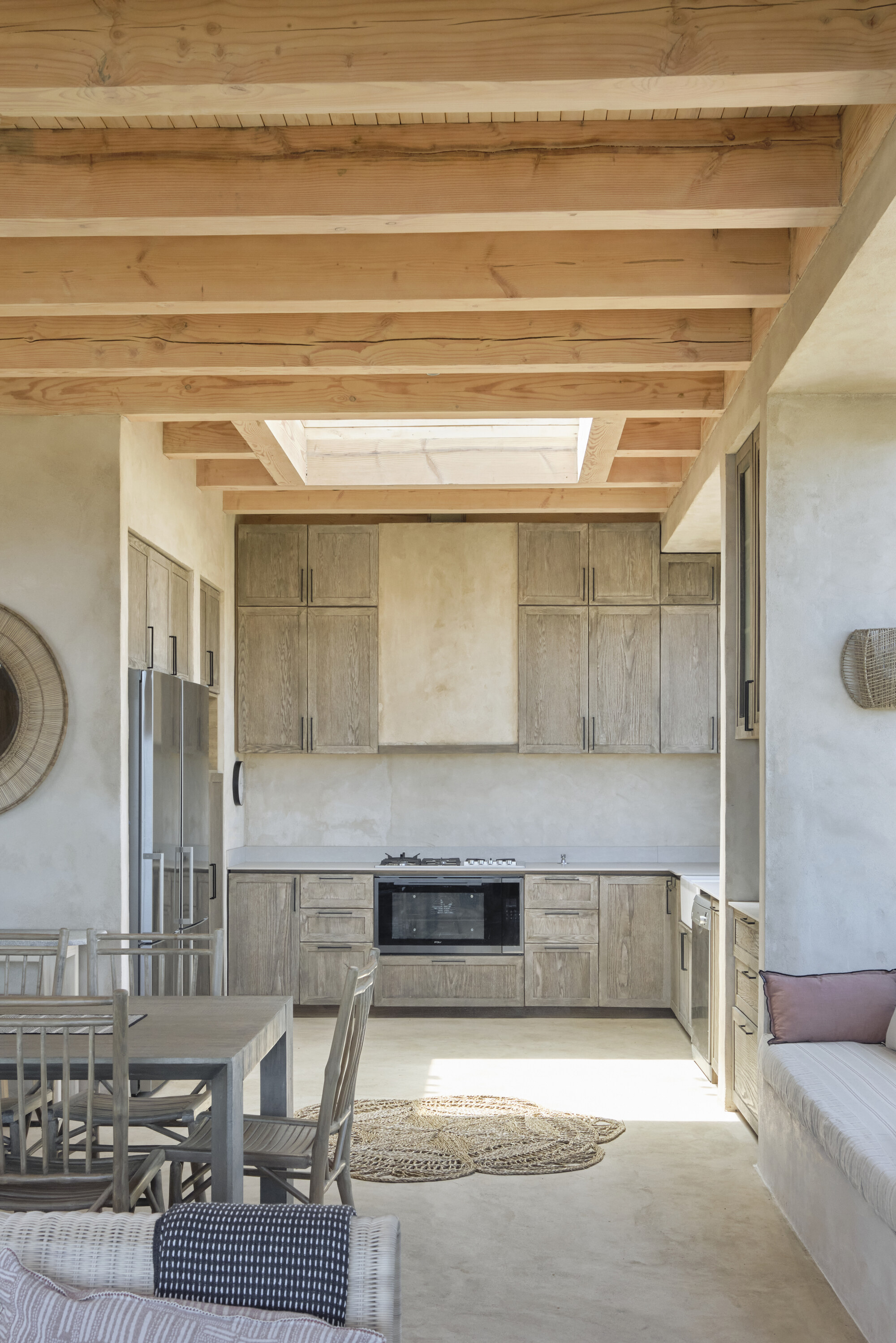 Open kitchen with weathered oak cabinets, exposed timber beams and a skylight, a round jute rug on the floor