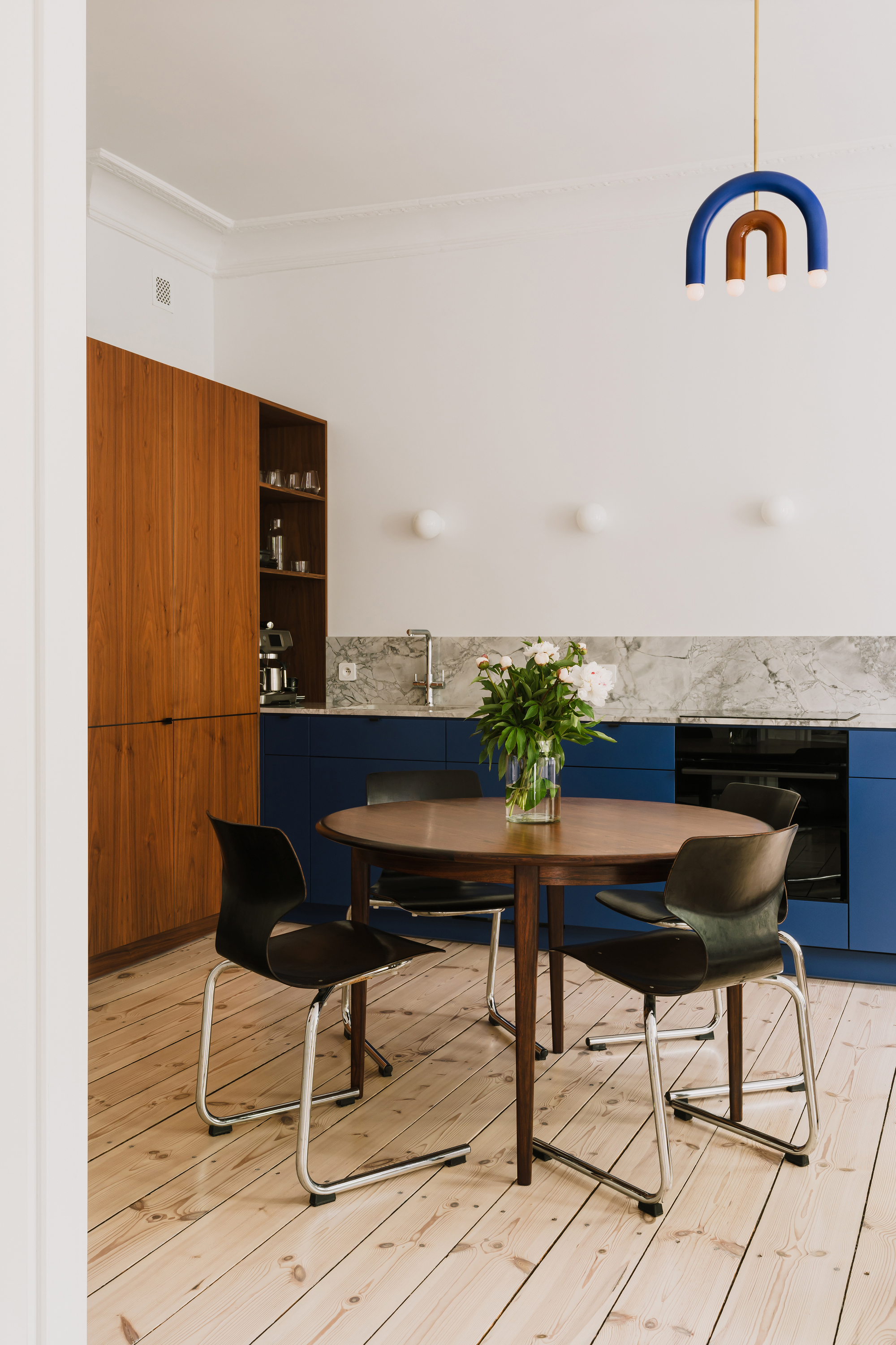 Vertical view of the dining table with a vase of white flowers, a blue arched pendant lamp hanging above