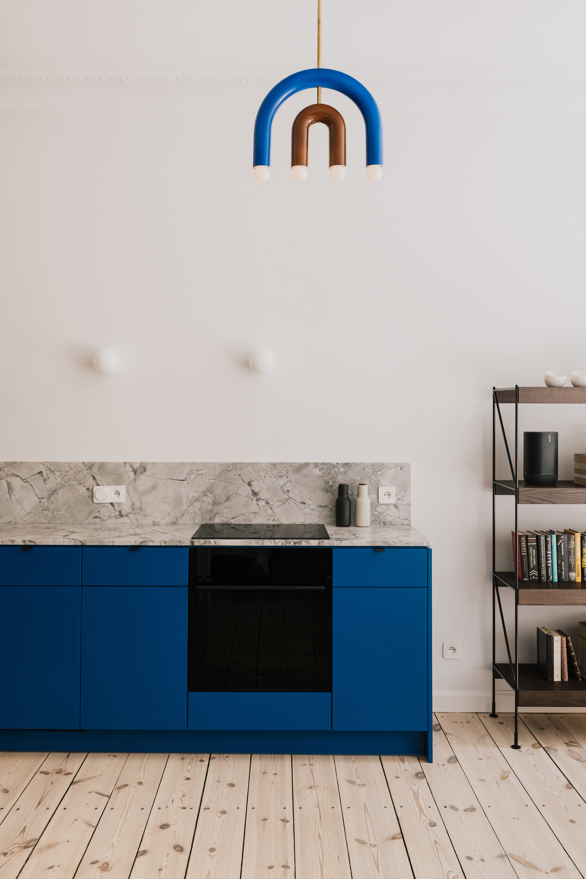 Blue cabinet run with black oven and induction hob under a marble backsplash and a blue and copper arched pendant