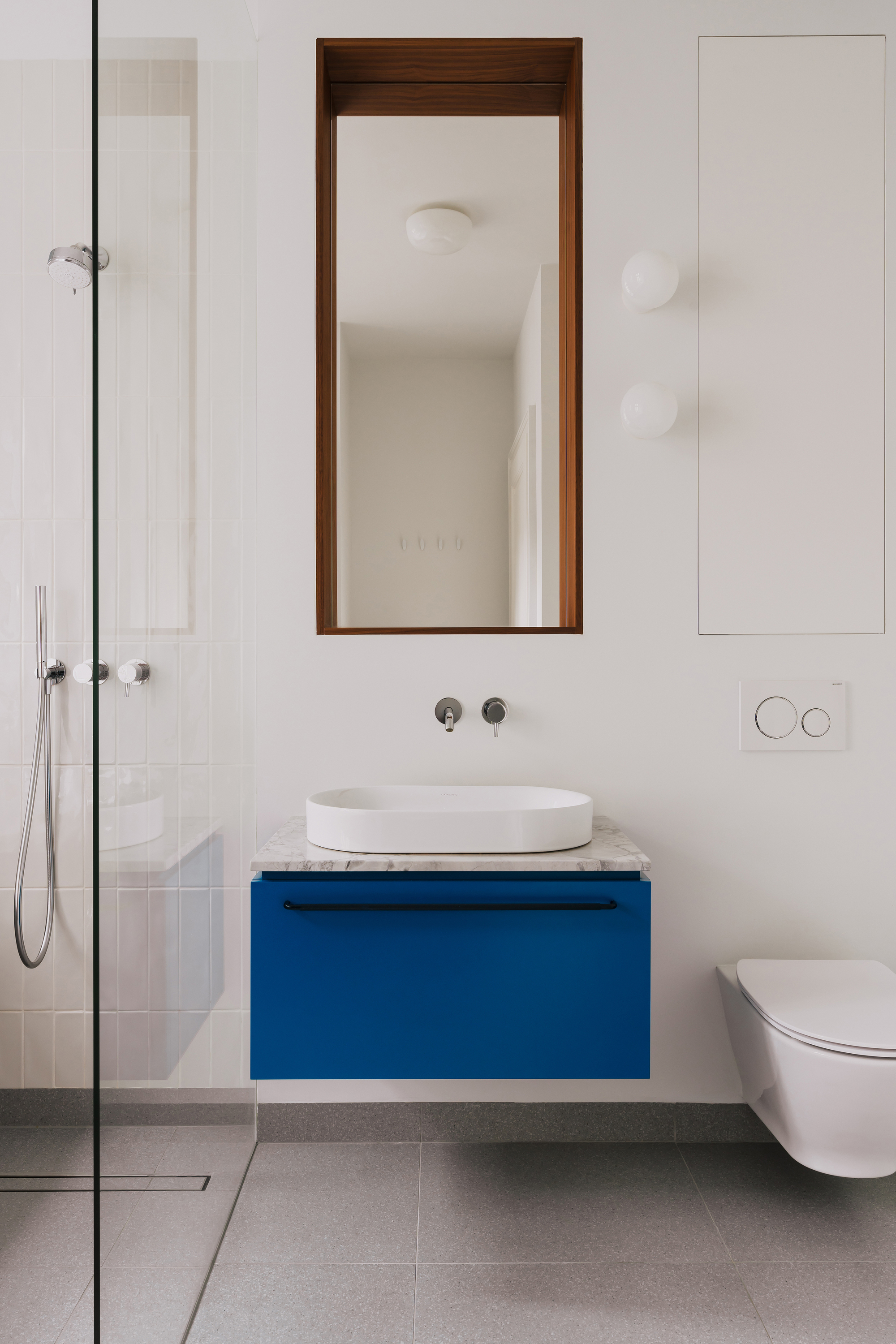 Bathroom vanity with a floating blue drawer, marble top and white basin beneath a walnut-framed mirror and two globe lights