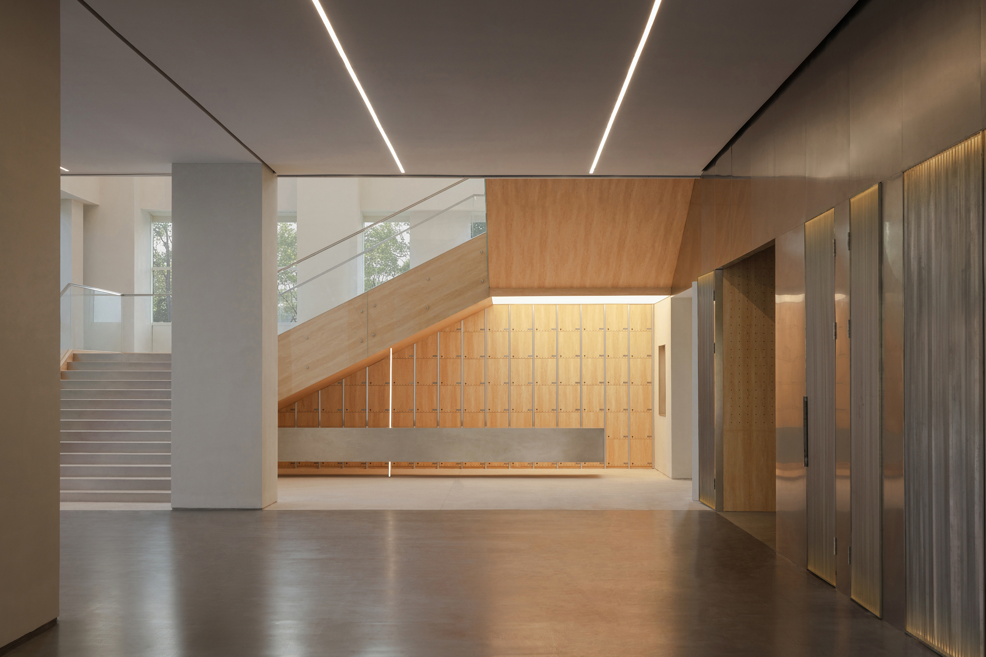 Entrance hall with a timber-clad staircase above wooden locker panels, beside a wall of metal mesh and lit vertical slots