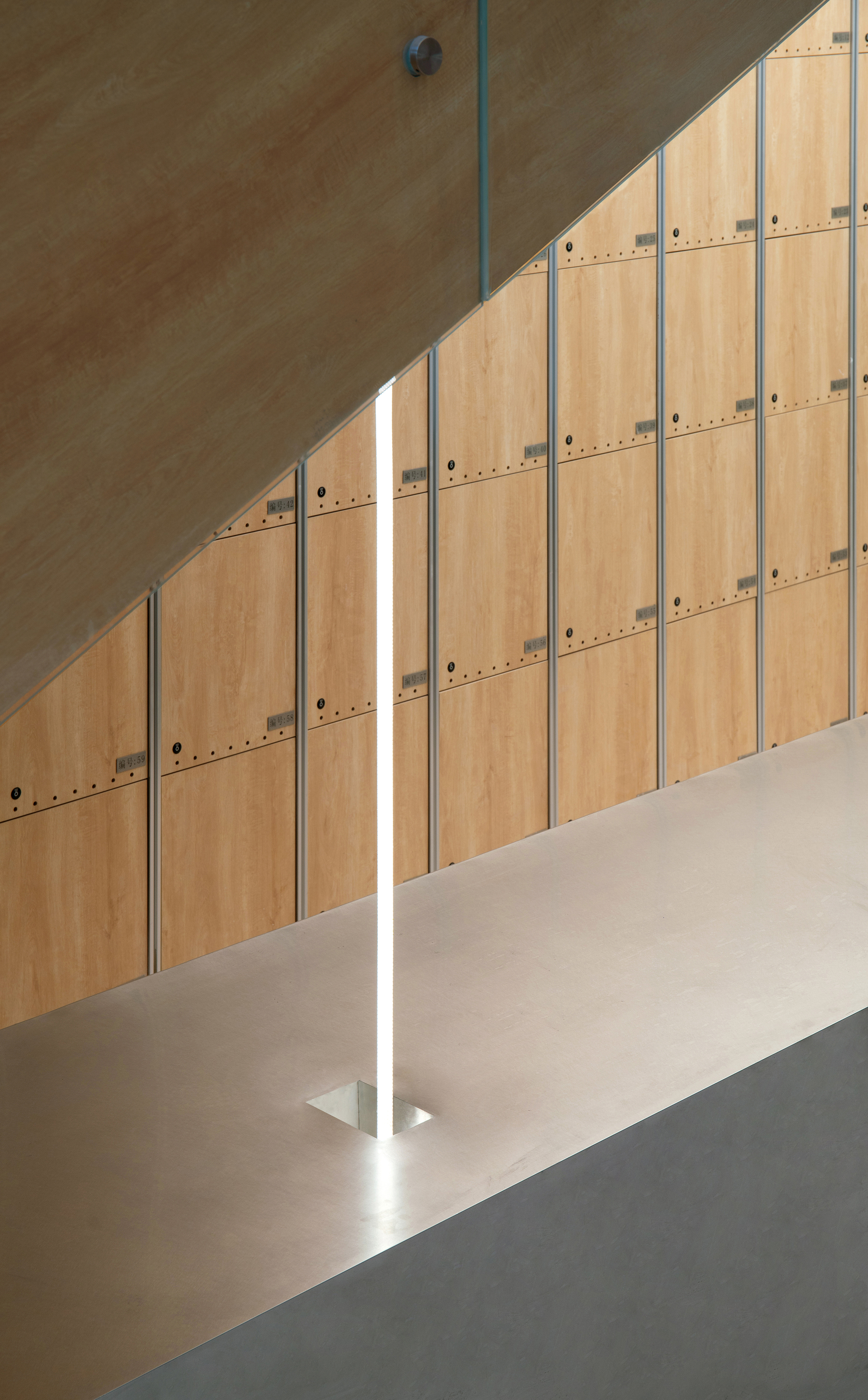 Wood-panelled locker wall beneath a sloped soffit, with a thin vertical strip of light rising from a metal floor plate