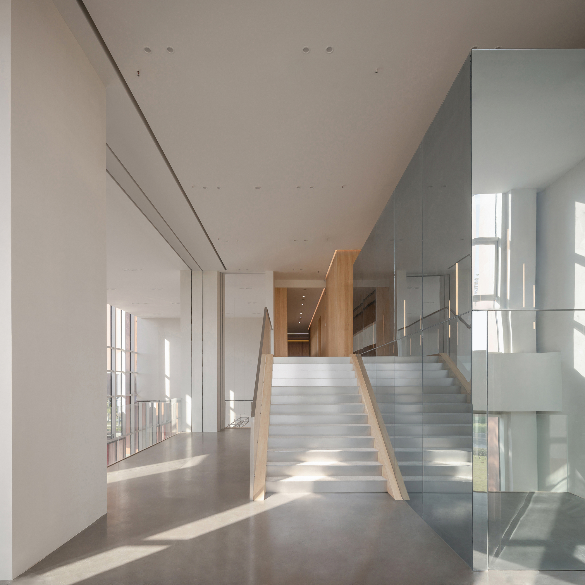 Wide stair with timber handrails leading to a wood-clad passage, beside a mirrored glass volume in low afternoon sun