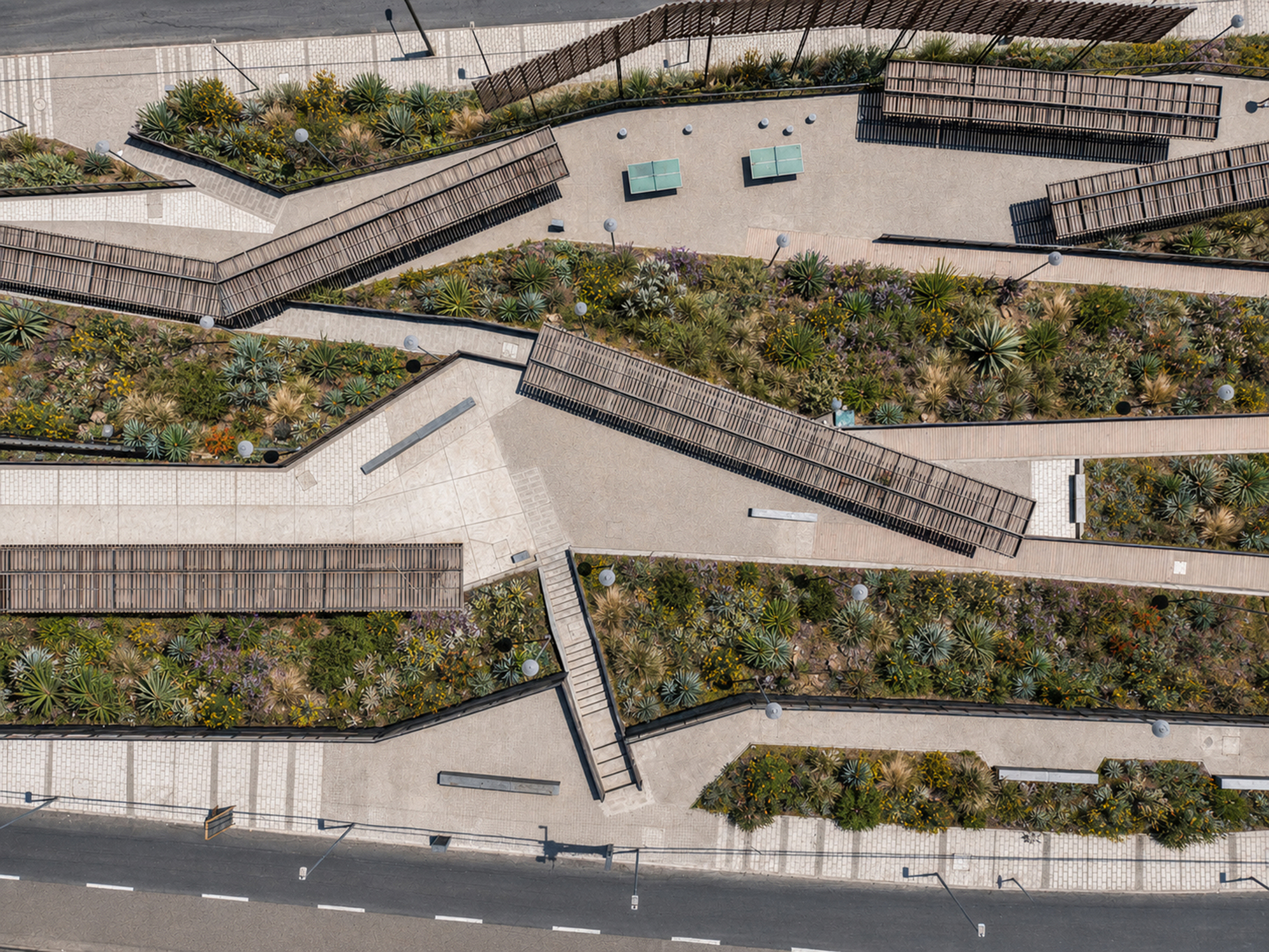 Aerial top-down view of zigzagging walkways, timber-slatted canopies and planted terraces of succulents and grasses between two roads