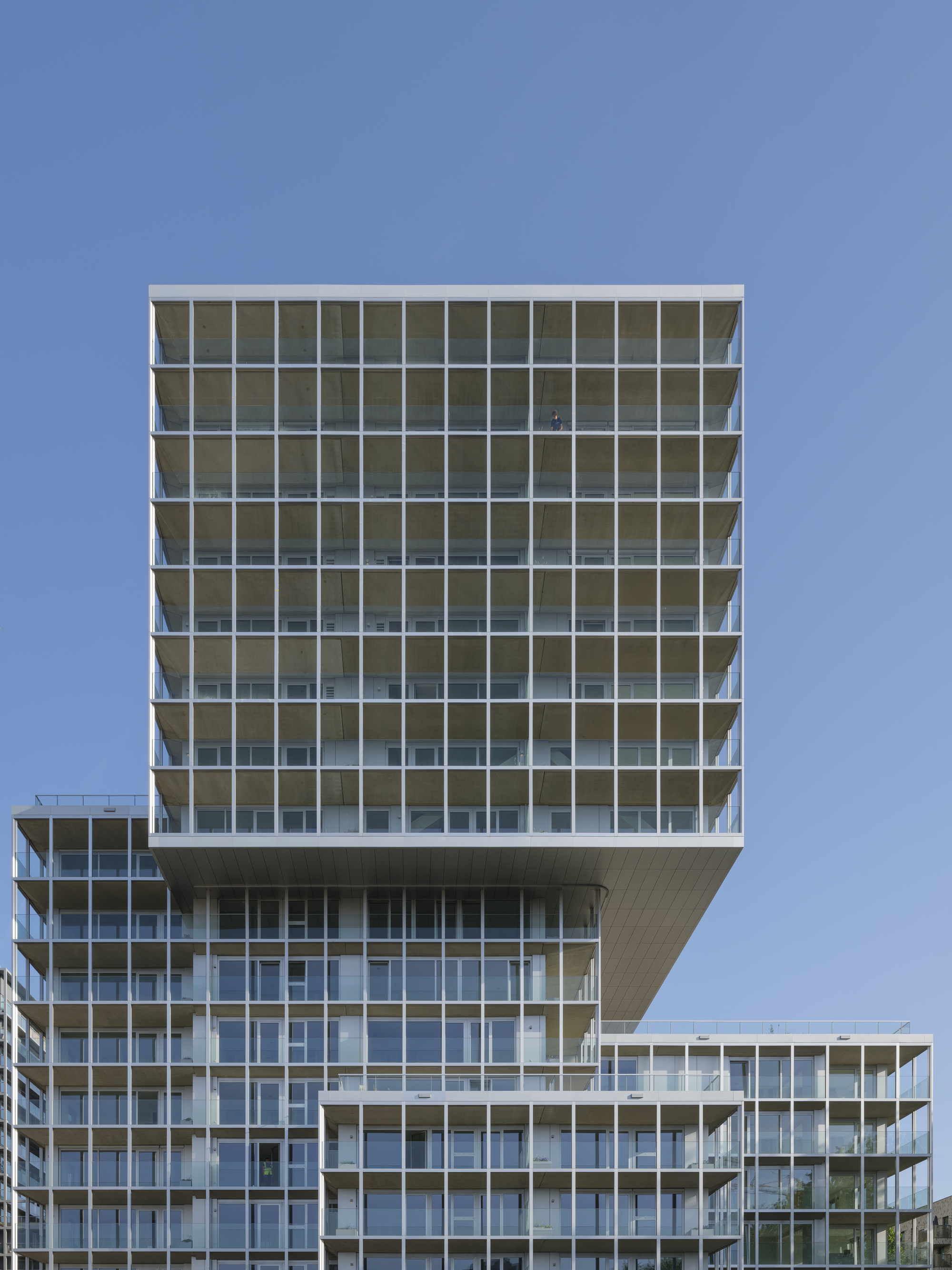 Cantilevered upper tower block with a white gridded balcony frame, seen against a clear blue sky