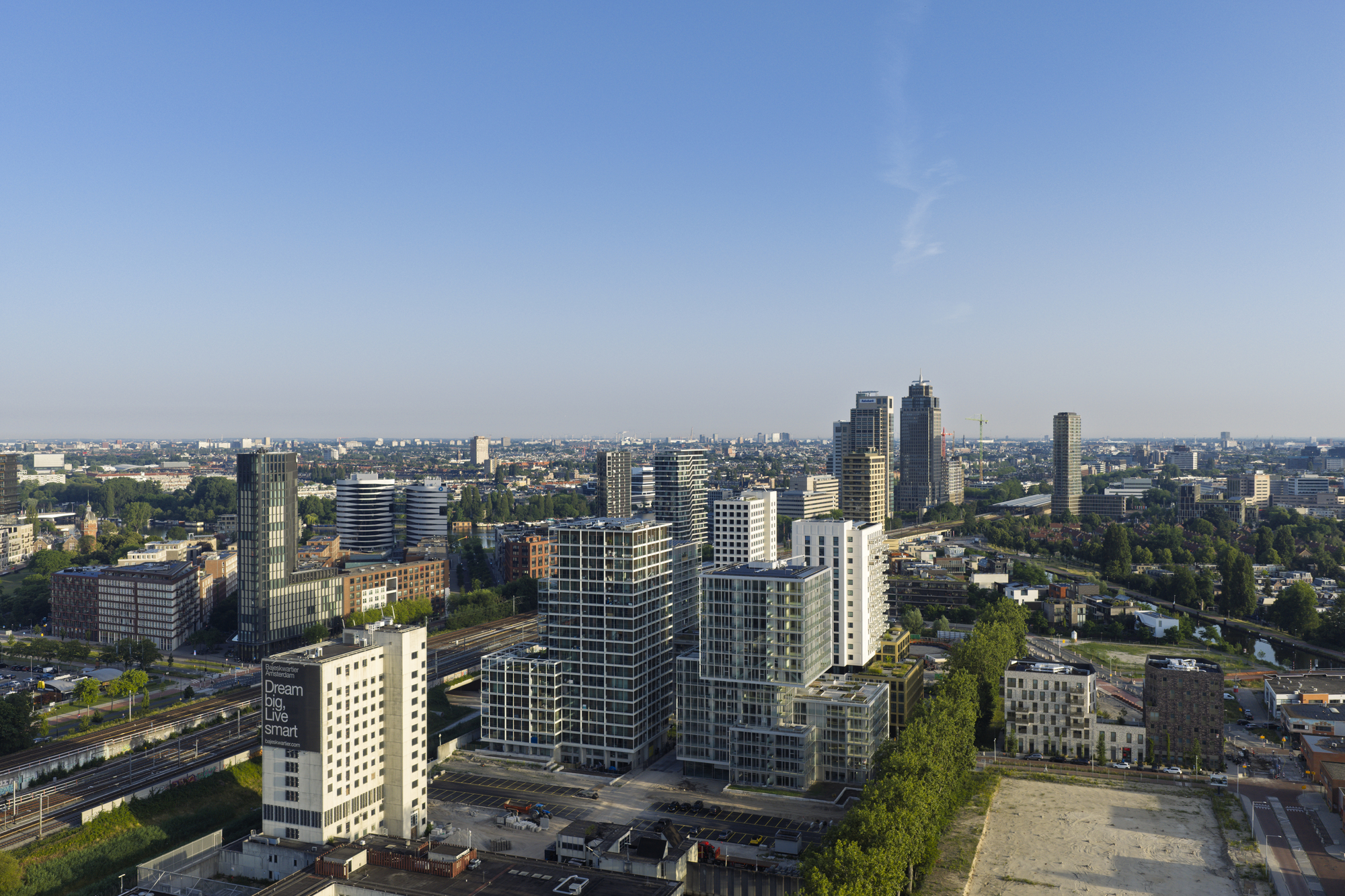 Aerial view of a cluster of mid-rise and high-rise towers beside rail tracks under a hazy morning sky