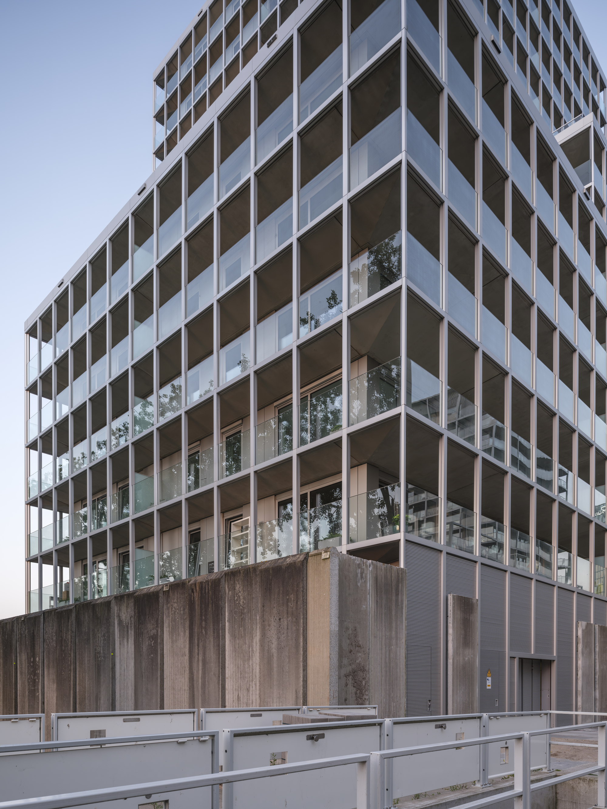 Base of the tower where a board-marked concrete wall meets glazed balcony bays and grey cladding, with a metal railing in front