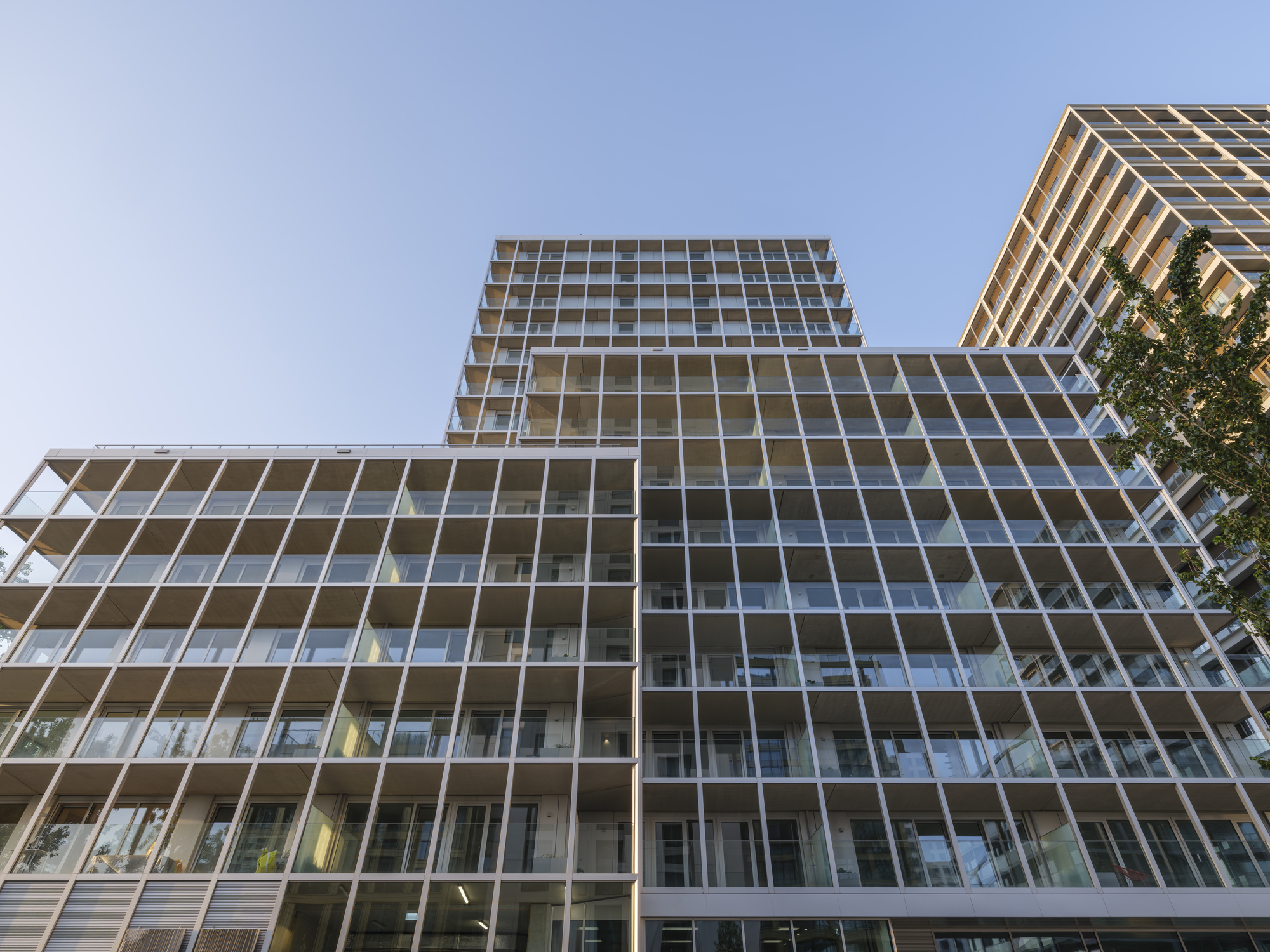 Low upward view of the white structural grid and glazed balconies of stepped tower volumes against a clear blue sky