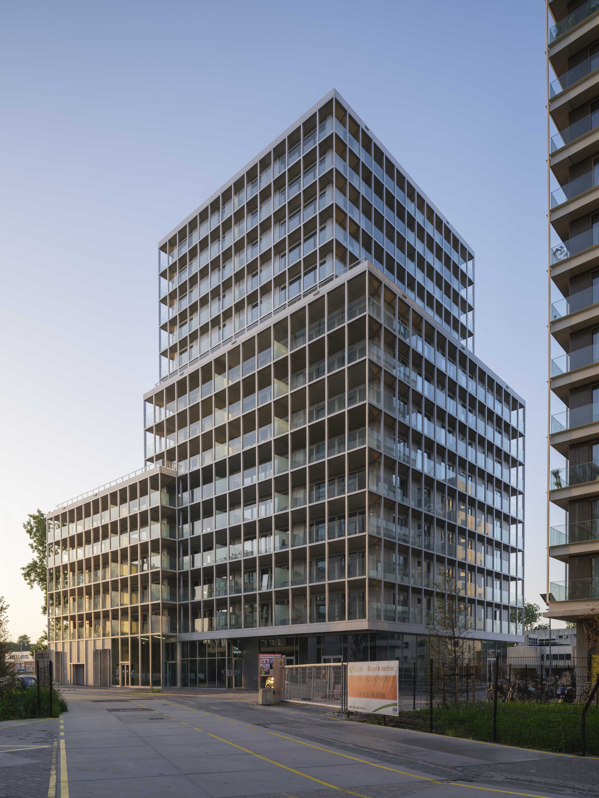 Stepped residential tower with gridded balcony facade rising above an empty street in clear blue dusk light
