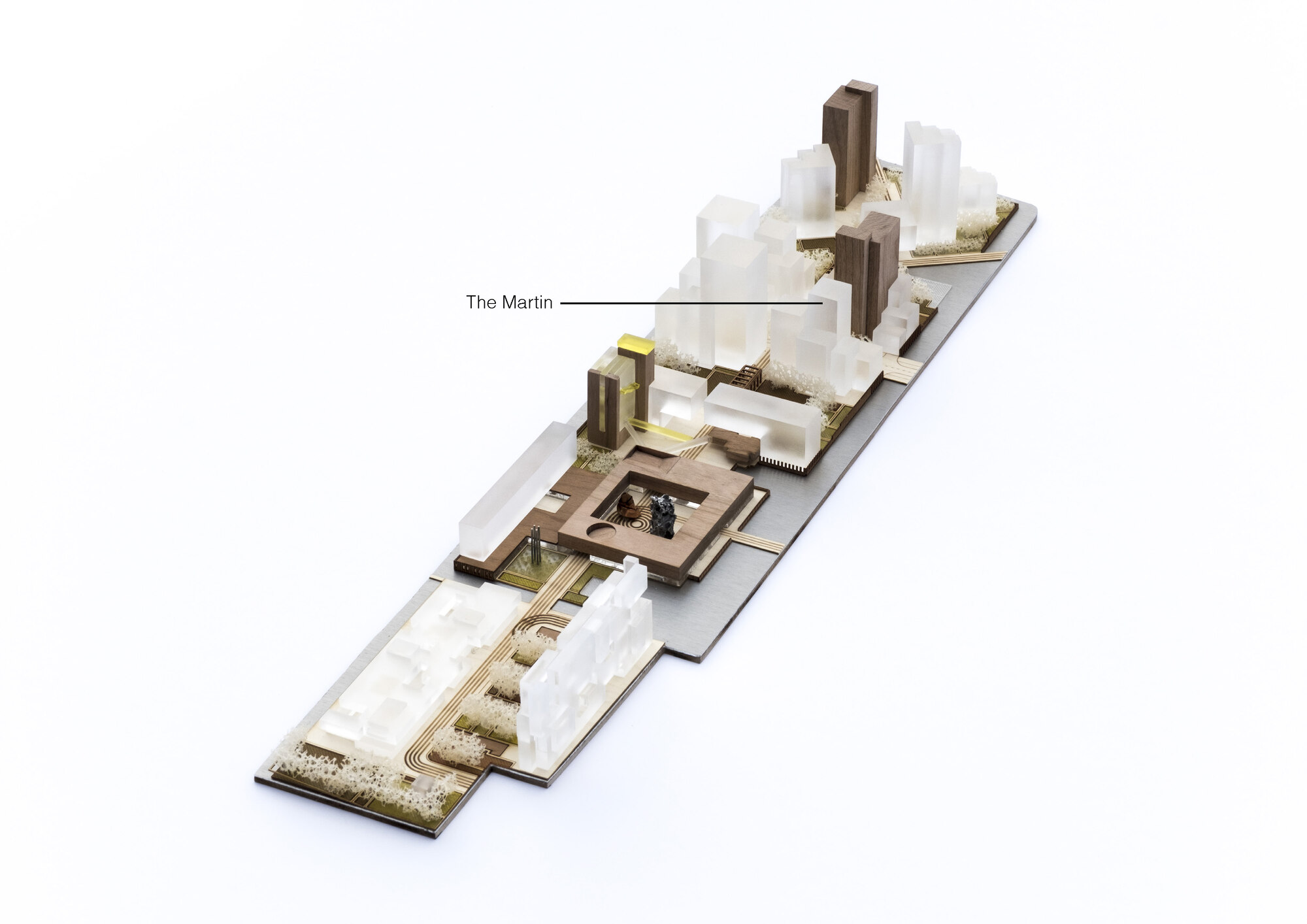 Aerial view of a physical site model with translucent white blocks, dark timber towers and a central courtyard building