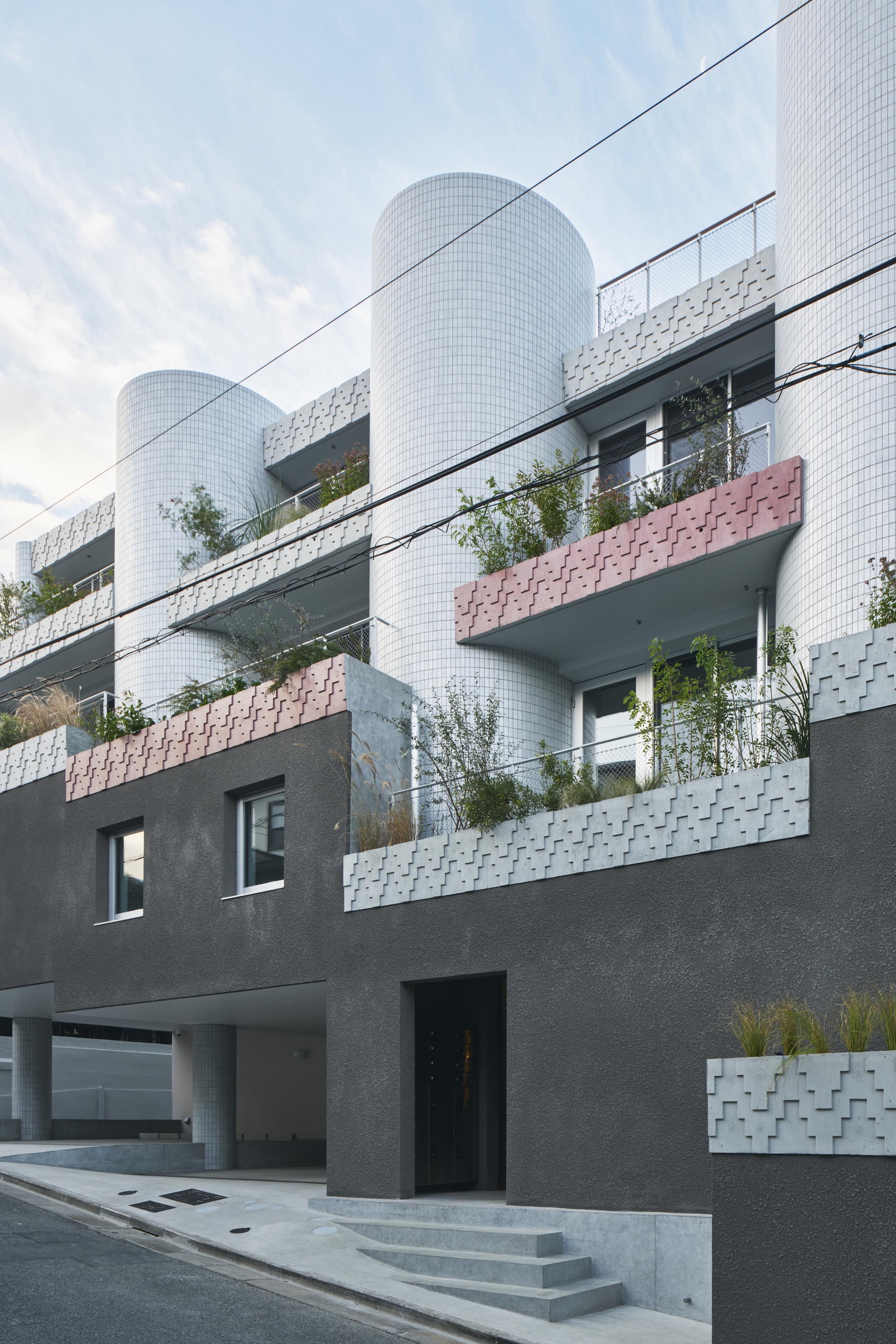 Tiled cylindrical bays and pink and white patterned planter edges rising above a dark stucco base with entry steps under soft cloud