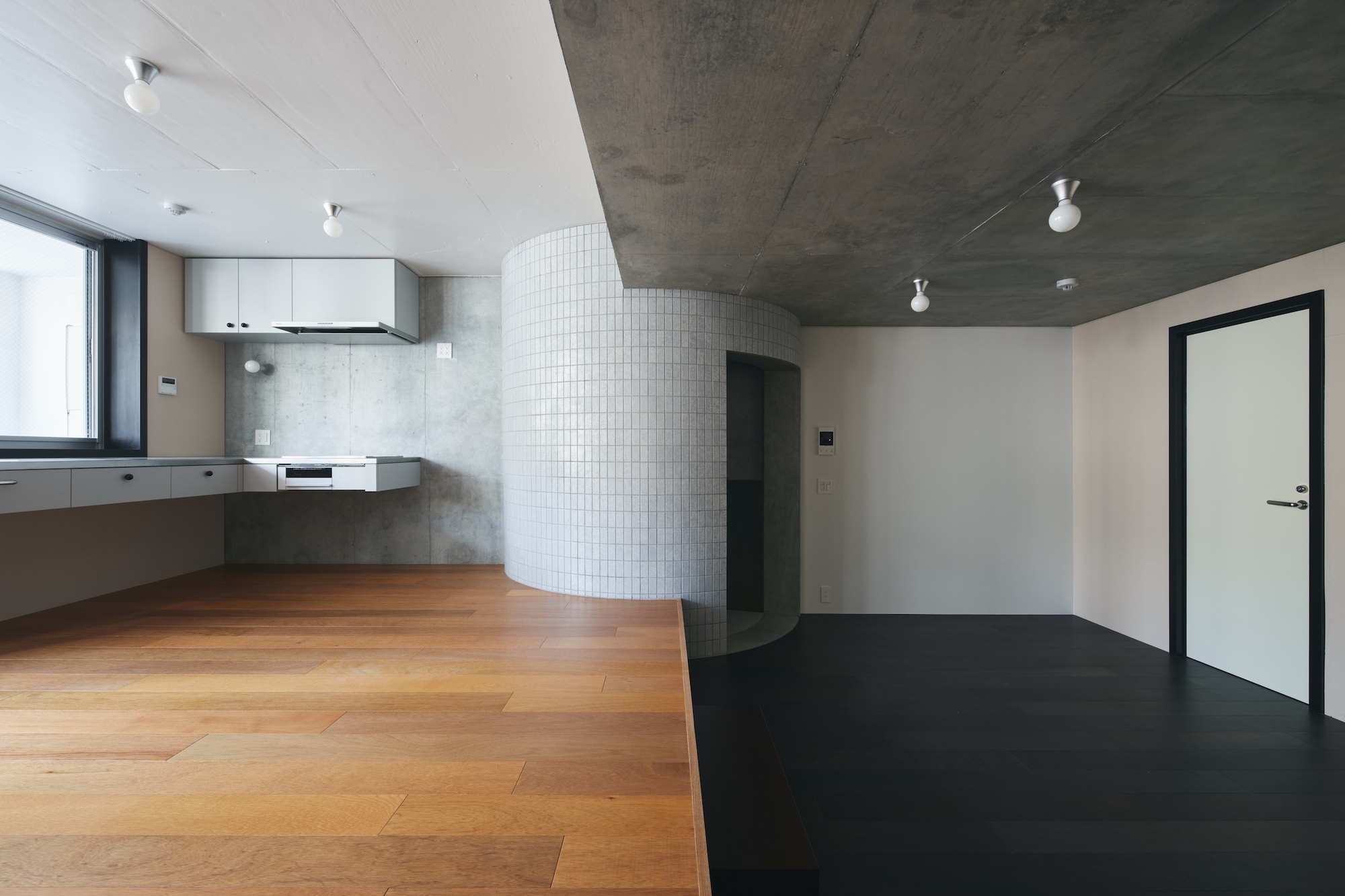 Open room with a curved white-tiled core dividing the raised timber kitchen floor from the dark-stained floor beside it