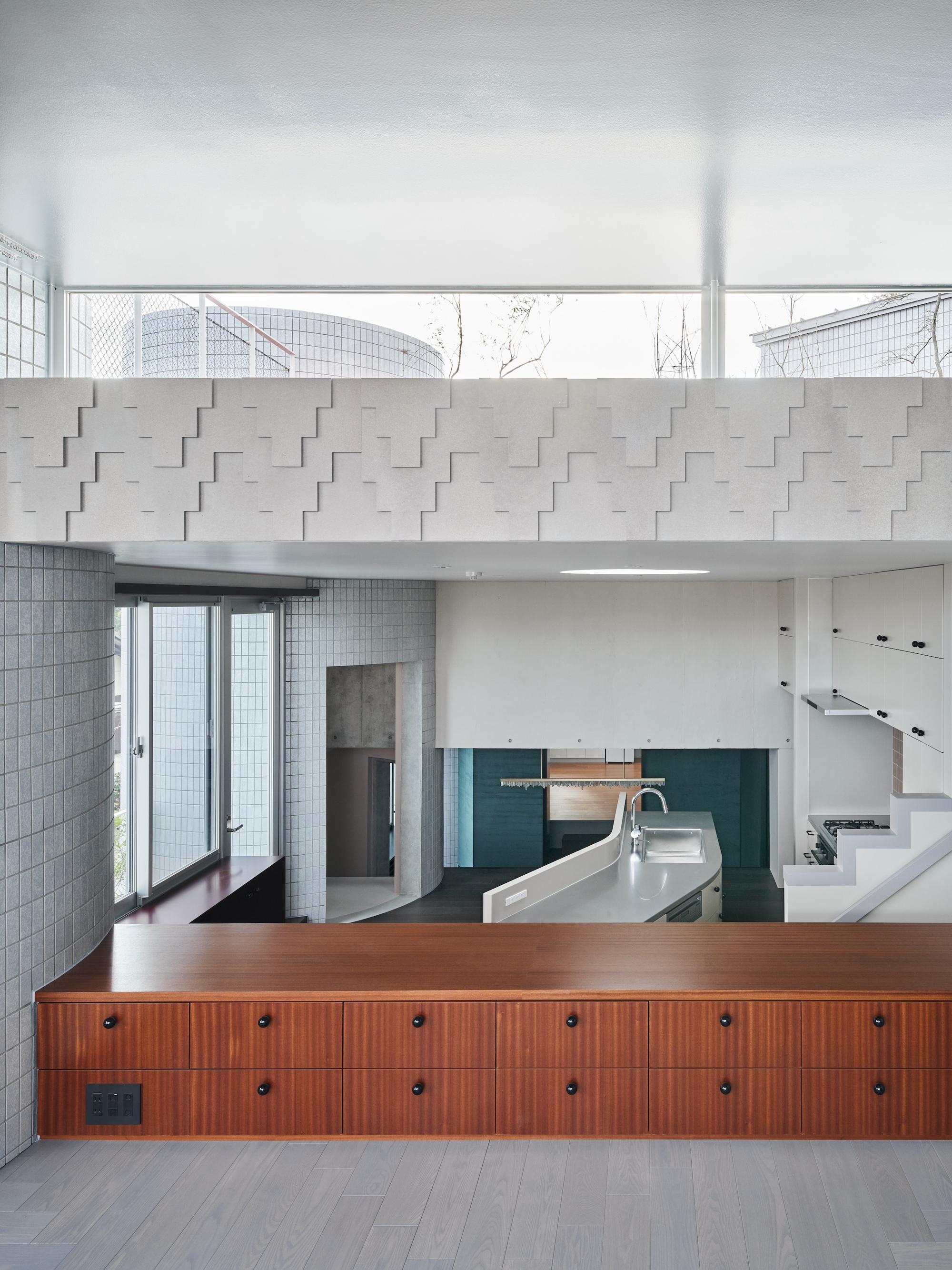 Mahogany drawer counter in front of a kitchen island, under a stepped white relief band and a clerestory with treetops