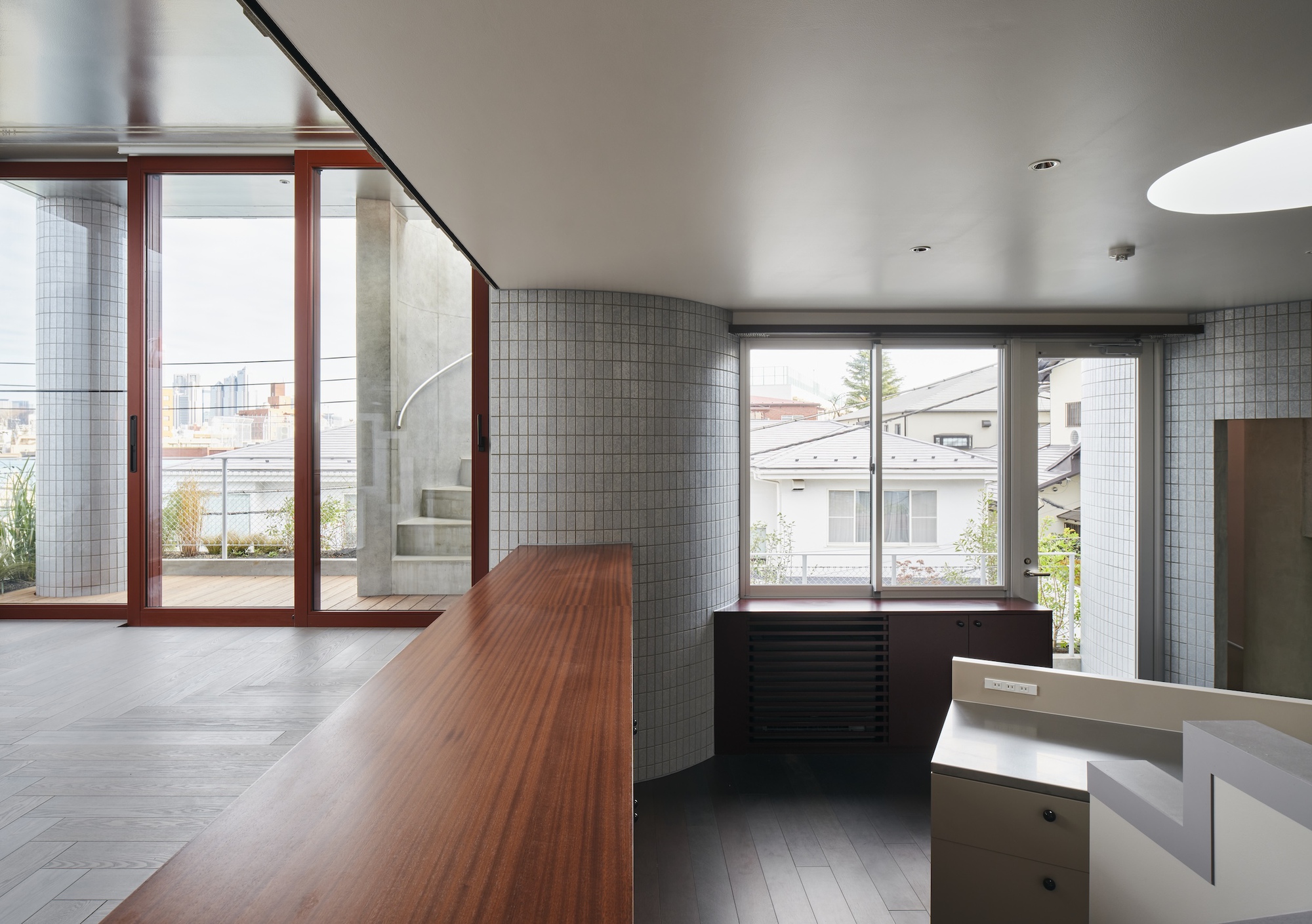 Long mahogany counter leading to red-framed glazing, curved tiled walls and a view over neighbouring rooftops on an overcast day