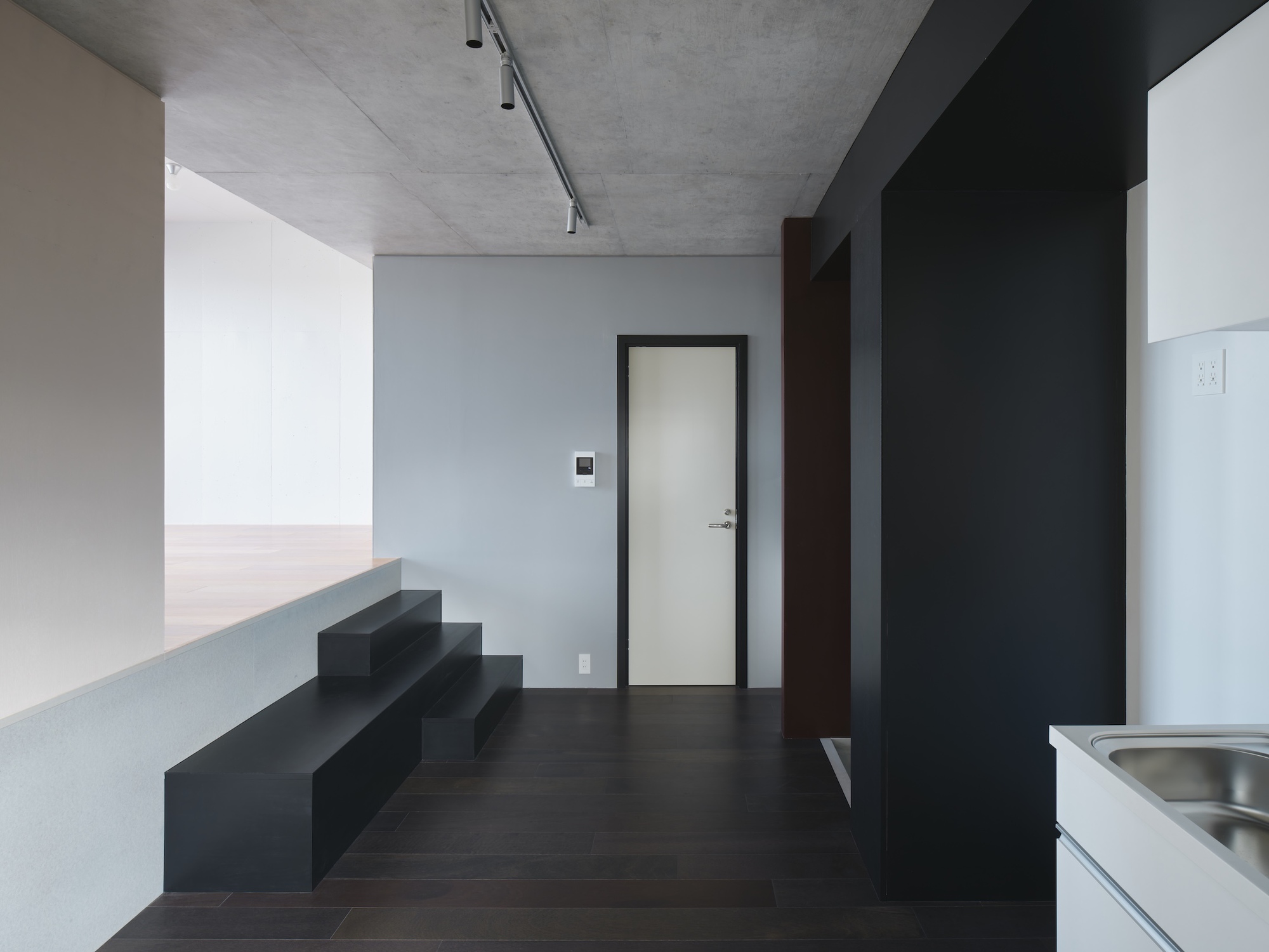 Open room with black stepped platform, dark timber floor and exposed concrete ceiling with a track light