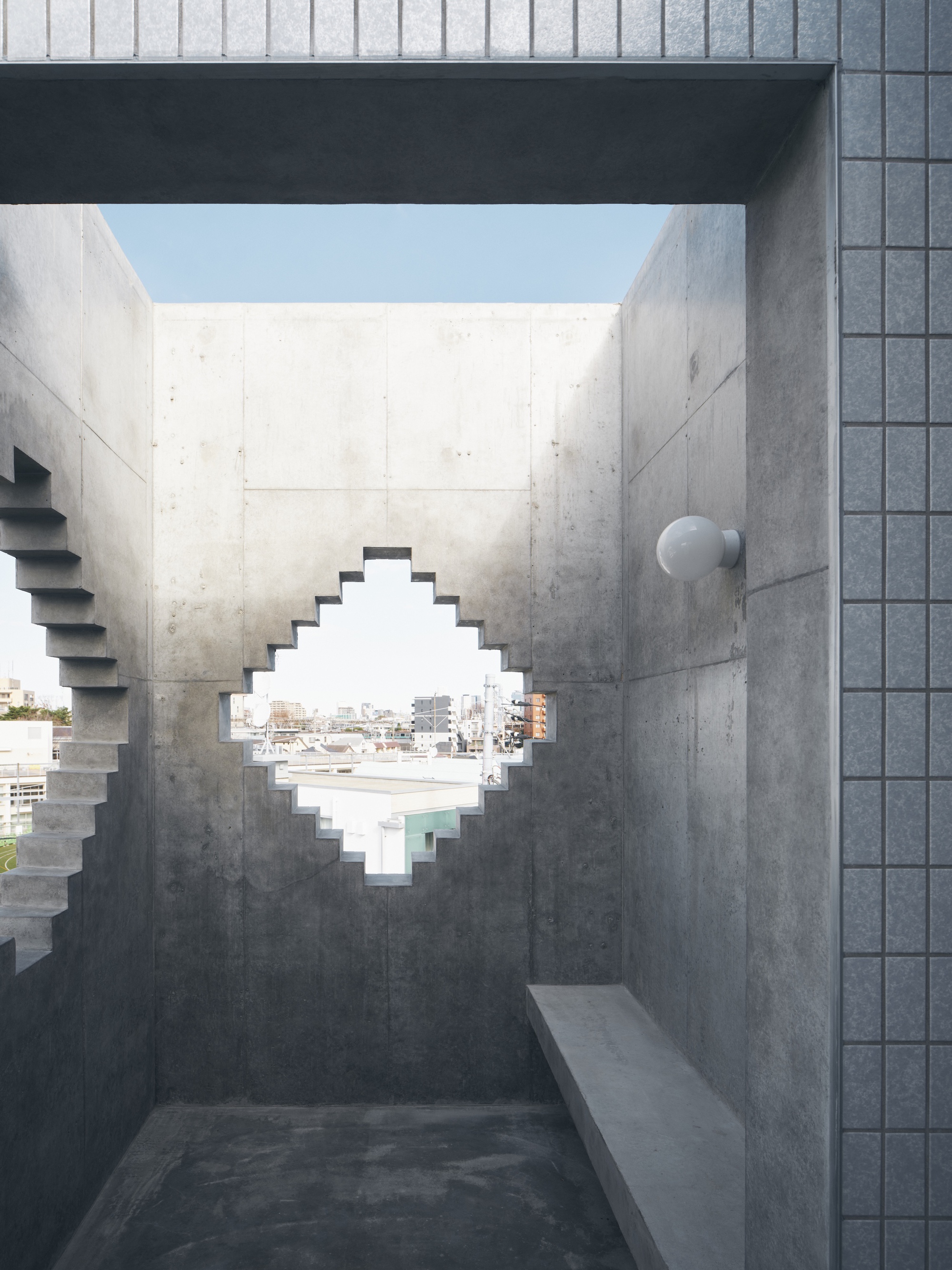 Concrete roof terrace with a stepped diamond-shaped opening framing rooftops under a pale blue sky