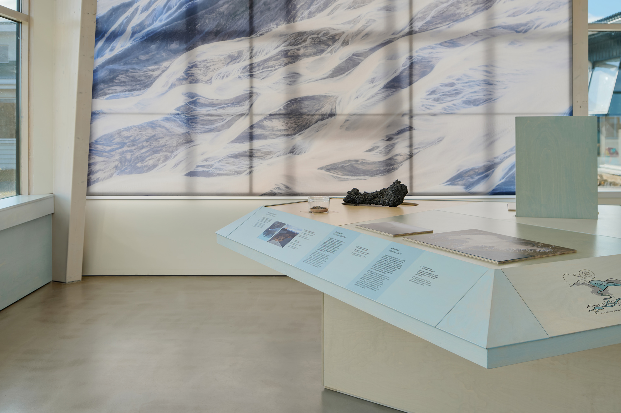 Sloped display table with text panels and a lava rock in front of a printed braided river image, in soft daylight