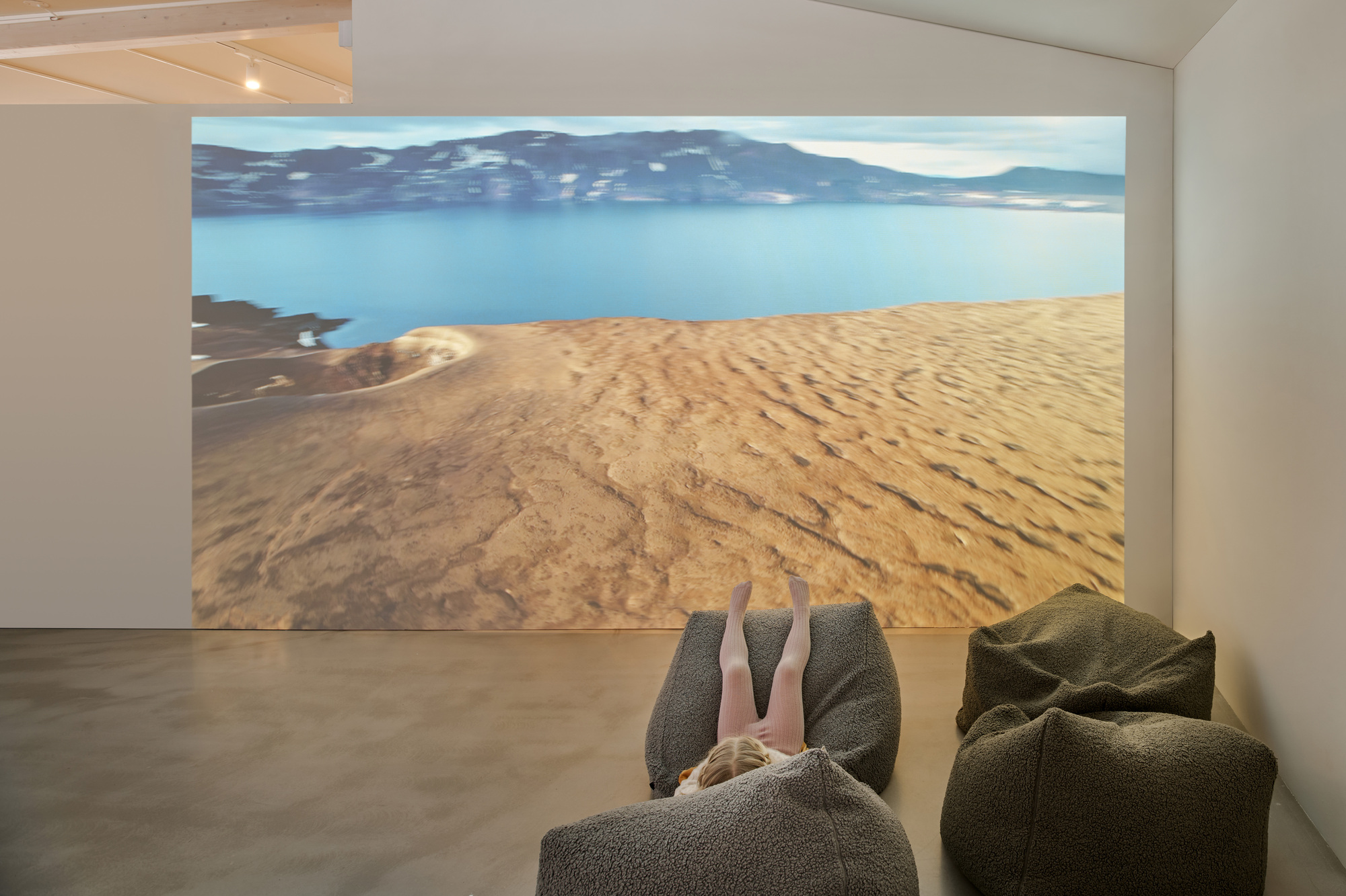 Child lying back on a grey bean bag in front of a projected crater lake and sandy slope