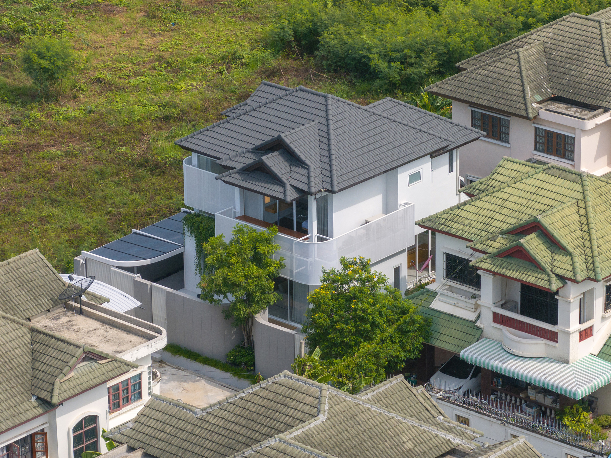 Aerial view of the grey tiled hipped roof and curved white balcony screens among neighbouring green-roofed houses