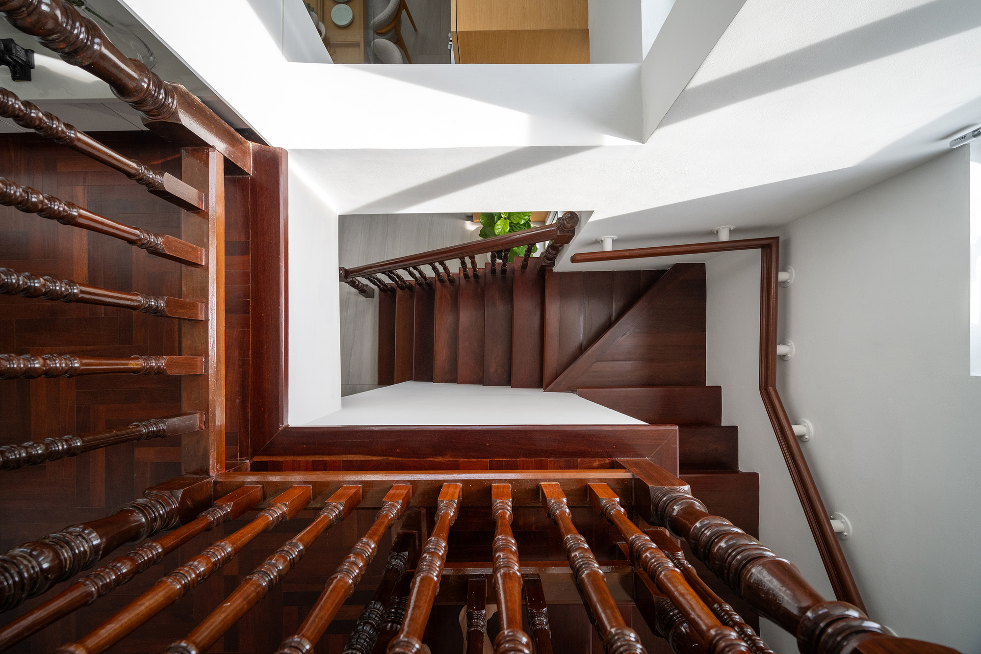 Looking straight down a stairwell of dark turned-wood balusters and handrails, with daylight washing the white walls