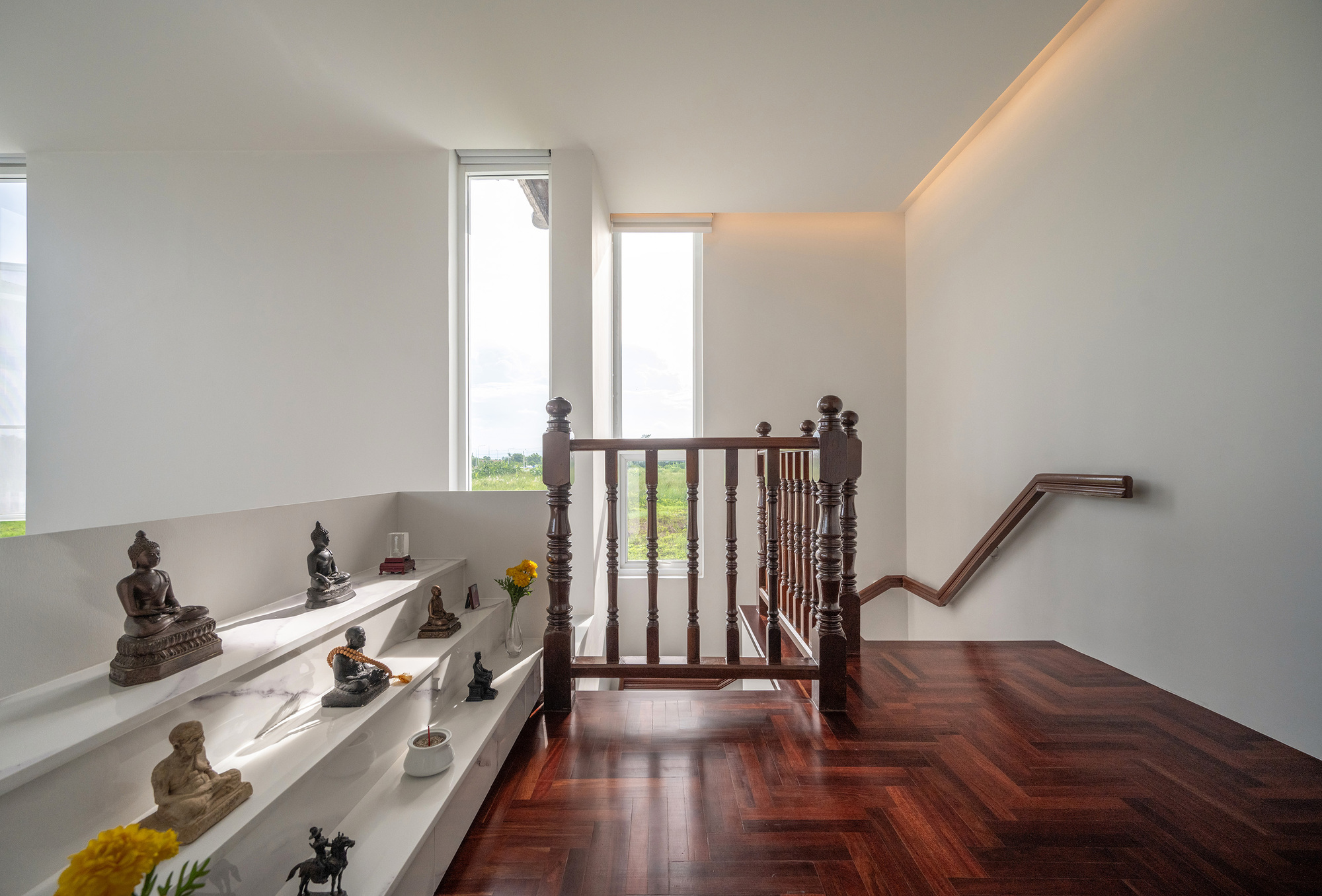 Stair landing with tiered white marble shelves holding small Buddha figures and marigolds beside a herringbone hardwood floor