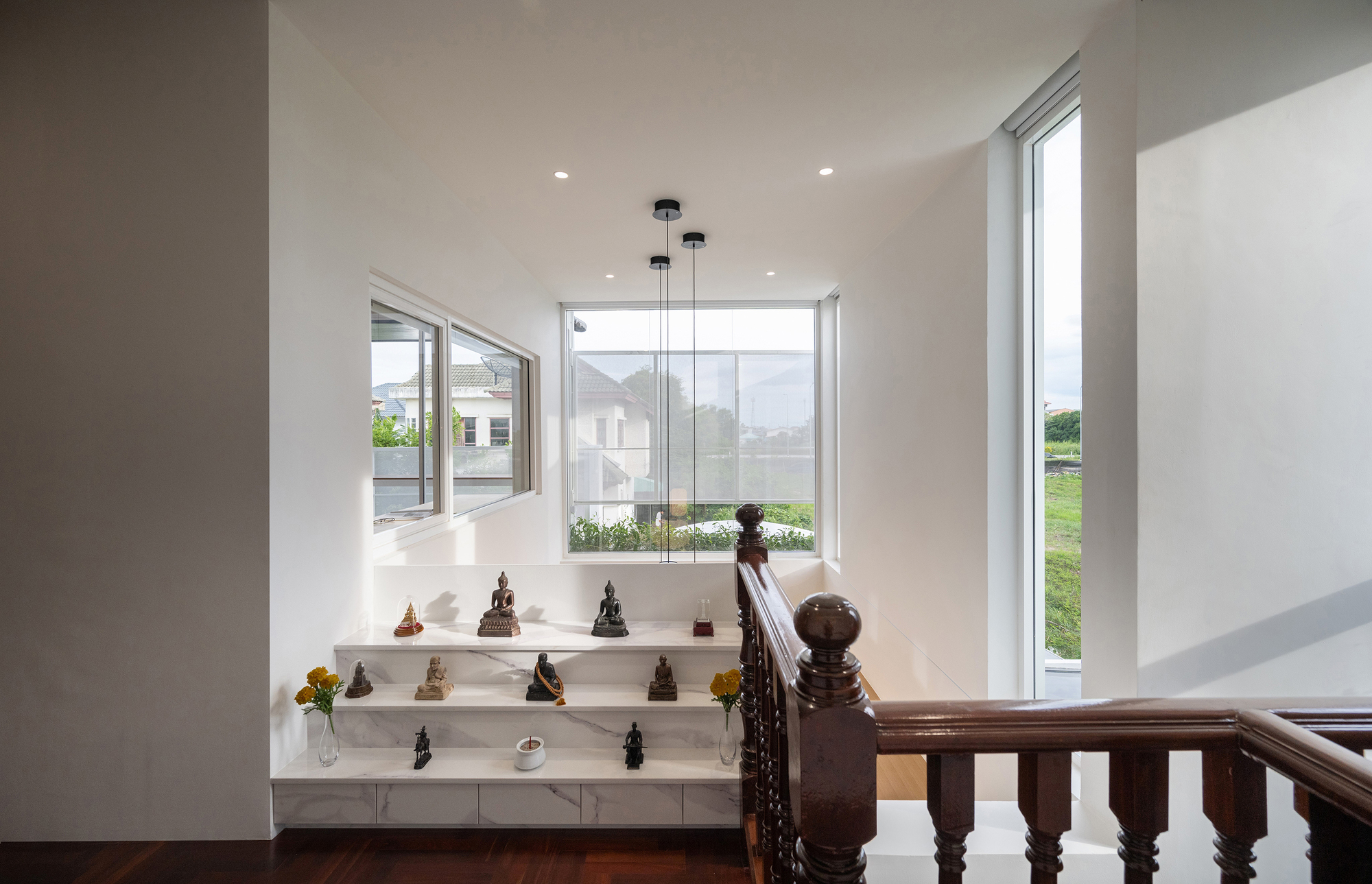 Marble altar steps with bronze Buddha figures and yellow flowers below a corner window that looks out to neighboring rooftops