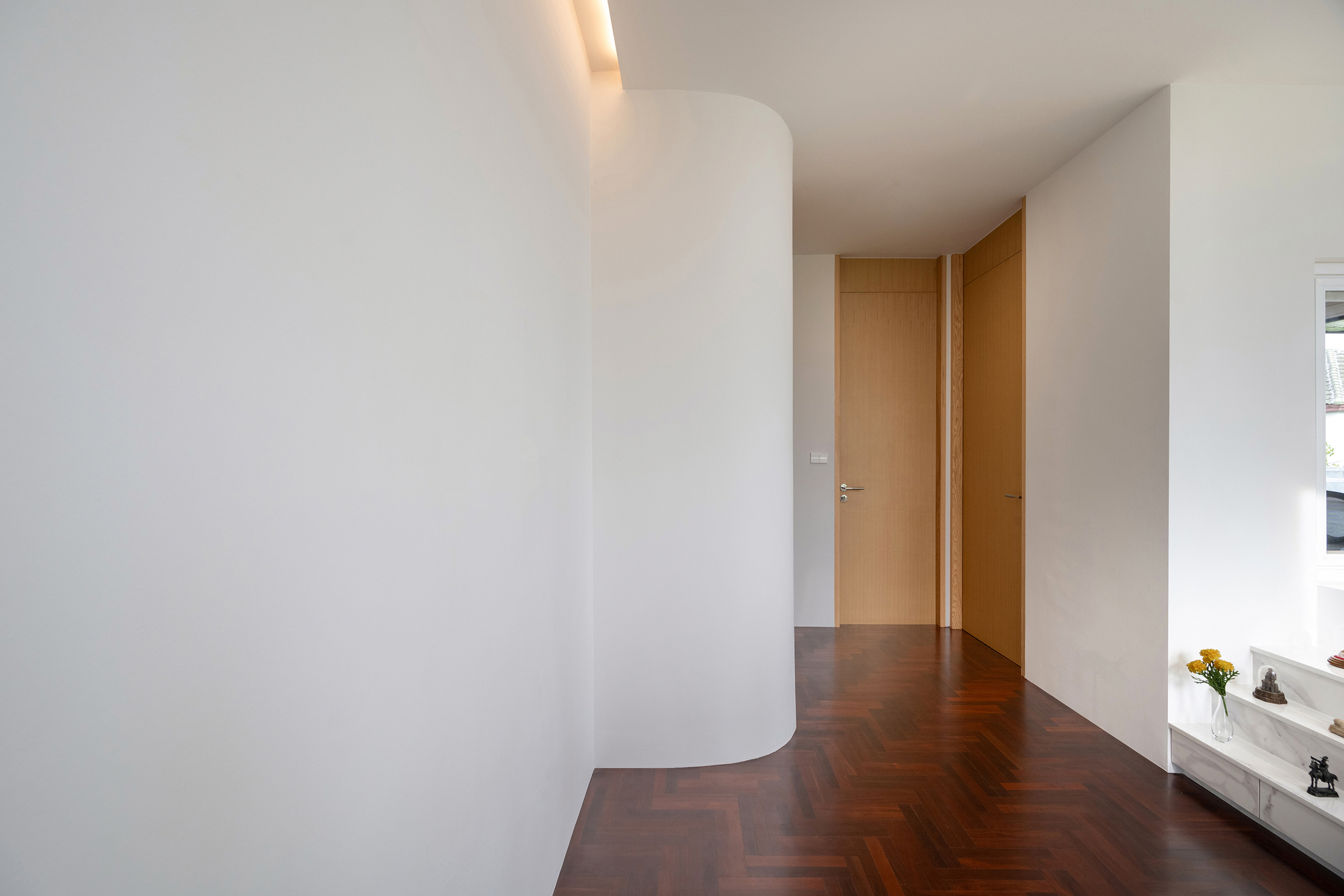 Upper hallway with a curved white wall, concealed cove light and pale timber doors at the end of a herringbone floor