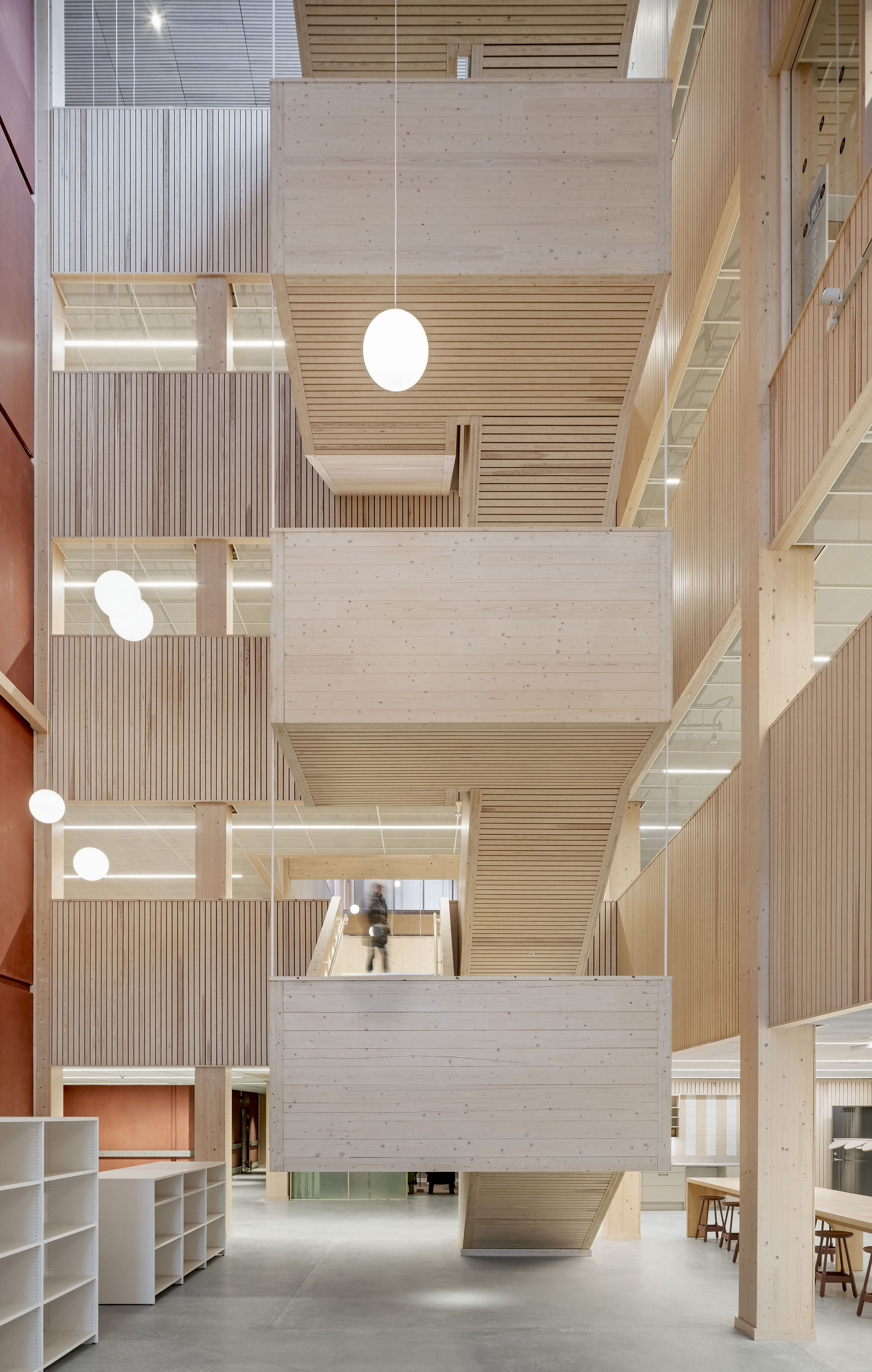 Timber atrium with stacked stair landings and globe pendant lights, one person climbing the flights beside a red wall