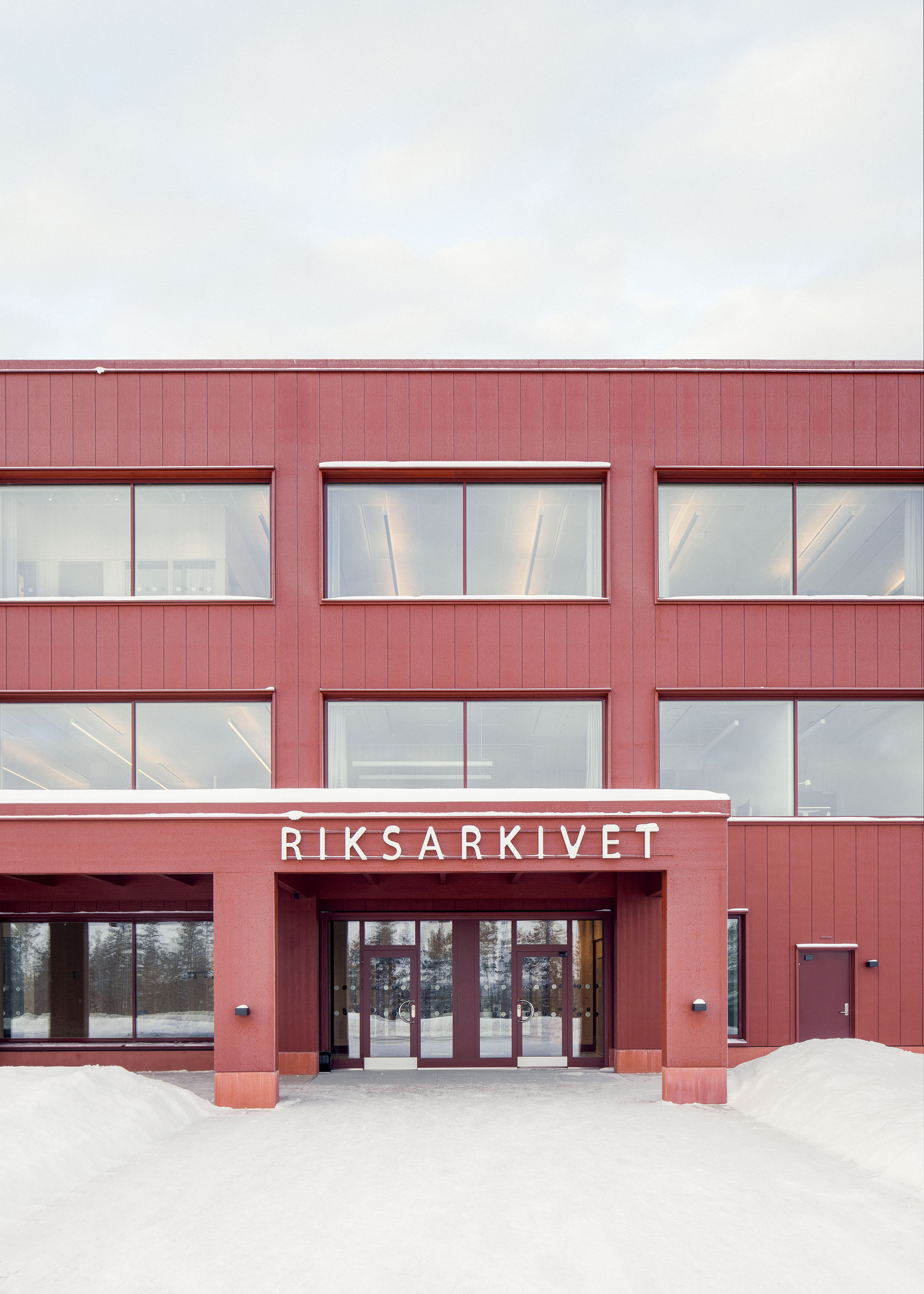 Entrance canopy with lettering over glazed double doors in a red panelled facade, snow banked in front