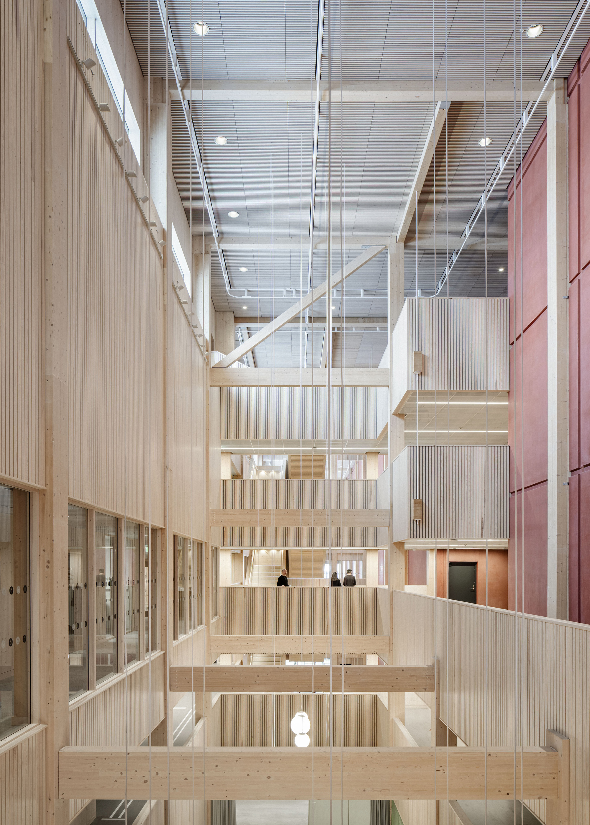 Looking up the timber atrium past slatted balconies, cross beams and a diagonal brace toward the grey ceiling