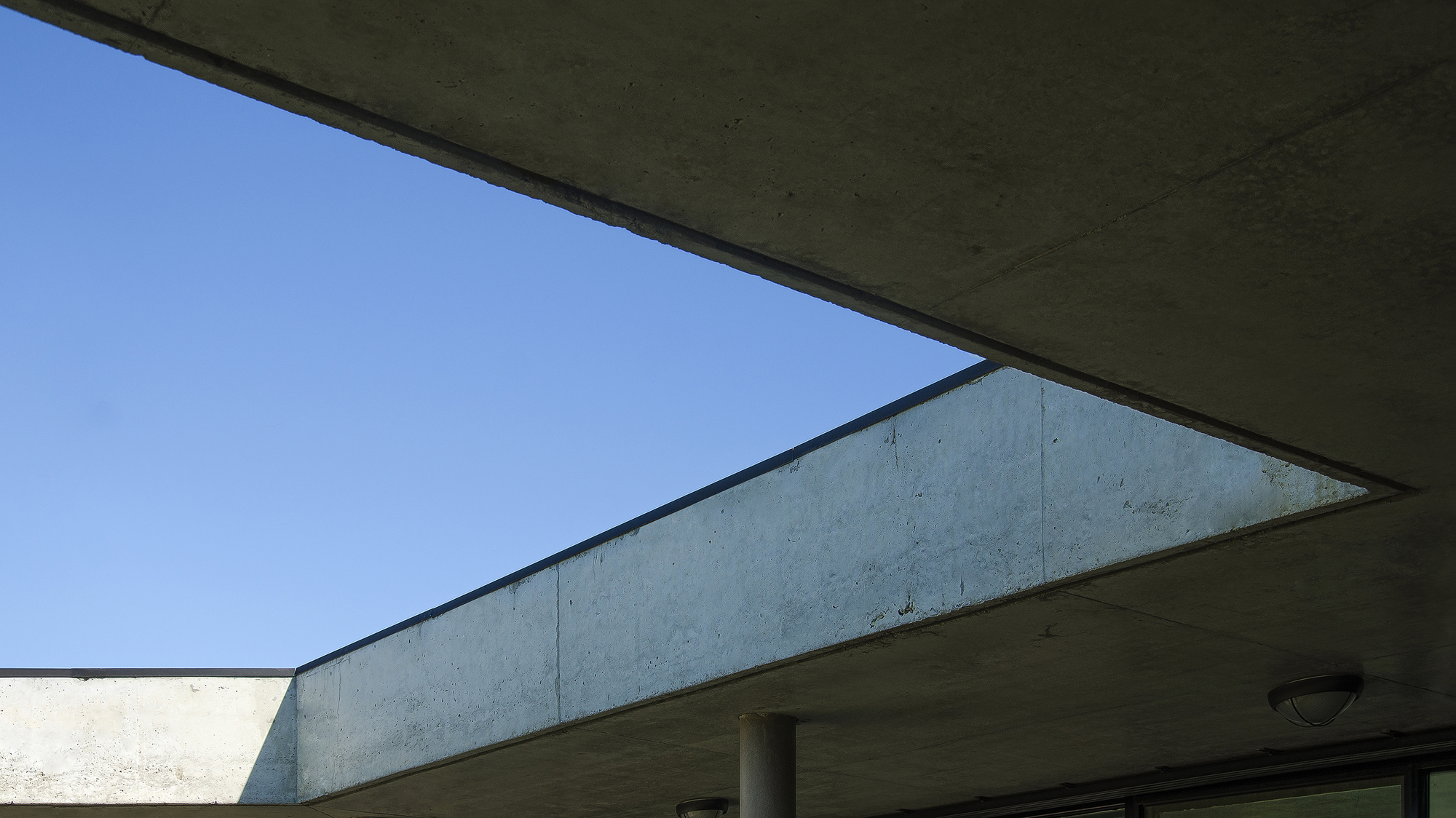 Upward view of the cantilevered concrete roof slab and a cylindrical column framing a sharp edge against a clear blue sky