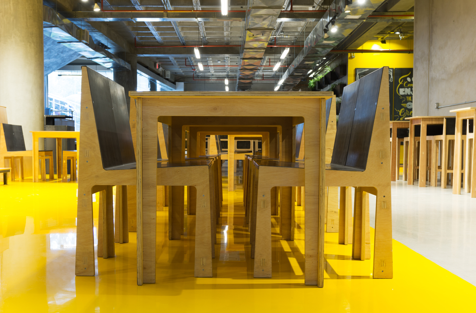 Low view of a plywood table and chairs with dark backrests on a glossy yellow resin floor