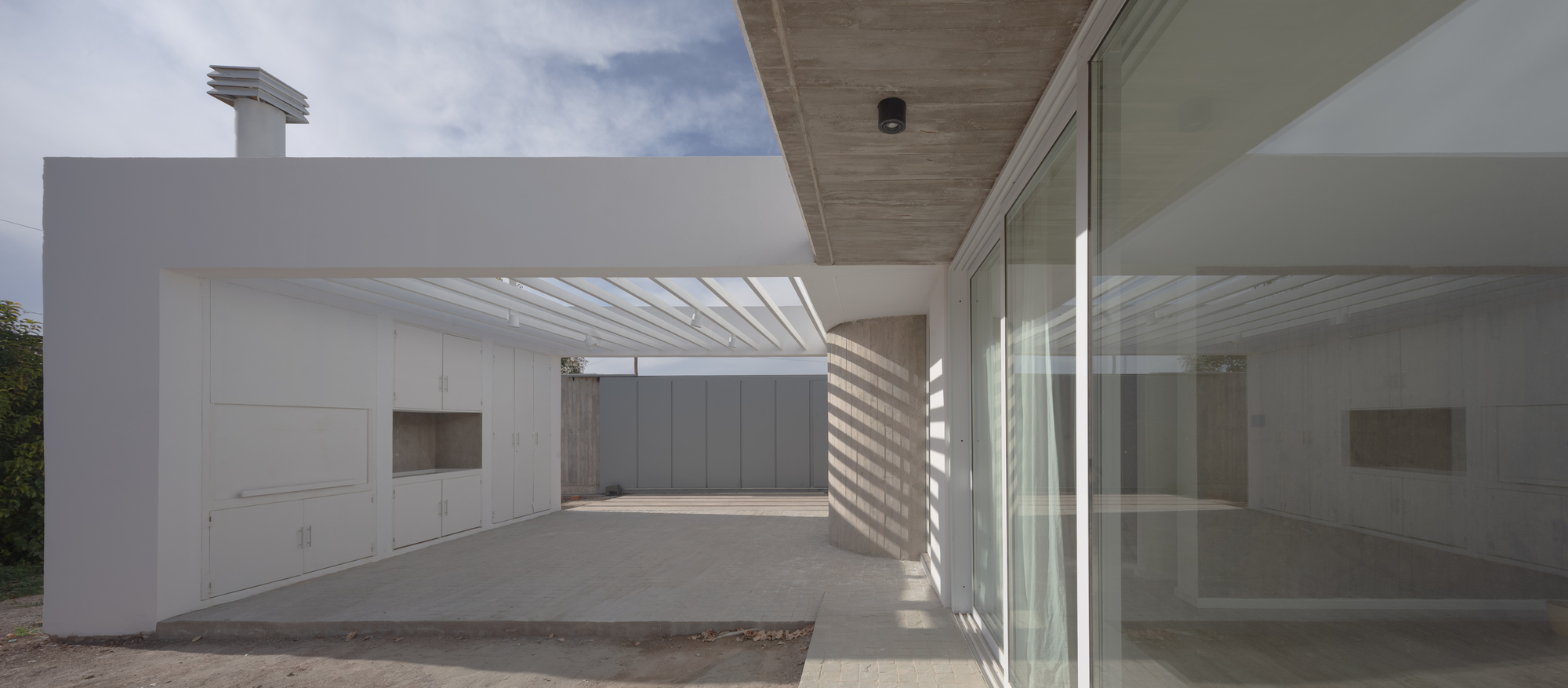 Covered terrace with white built-in cabinets, a round concrete column and a slatted pergola casting stripes of sunlight