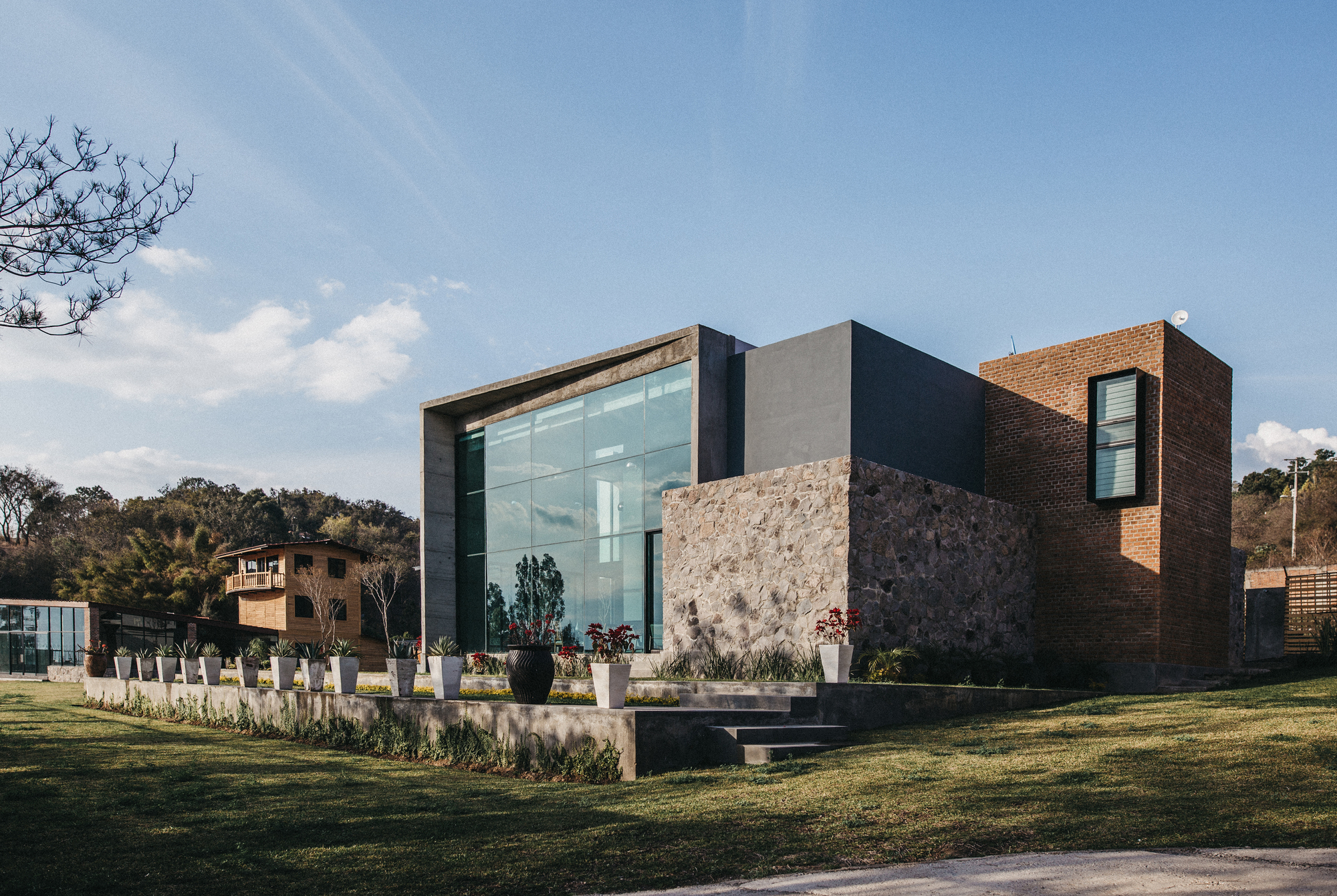 Side view of glass, stone and exposed brick volumes with a short stair rising from the lawn in late sun