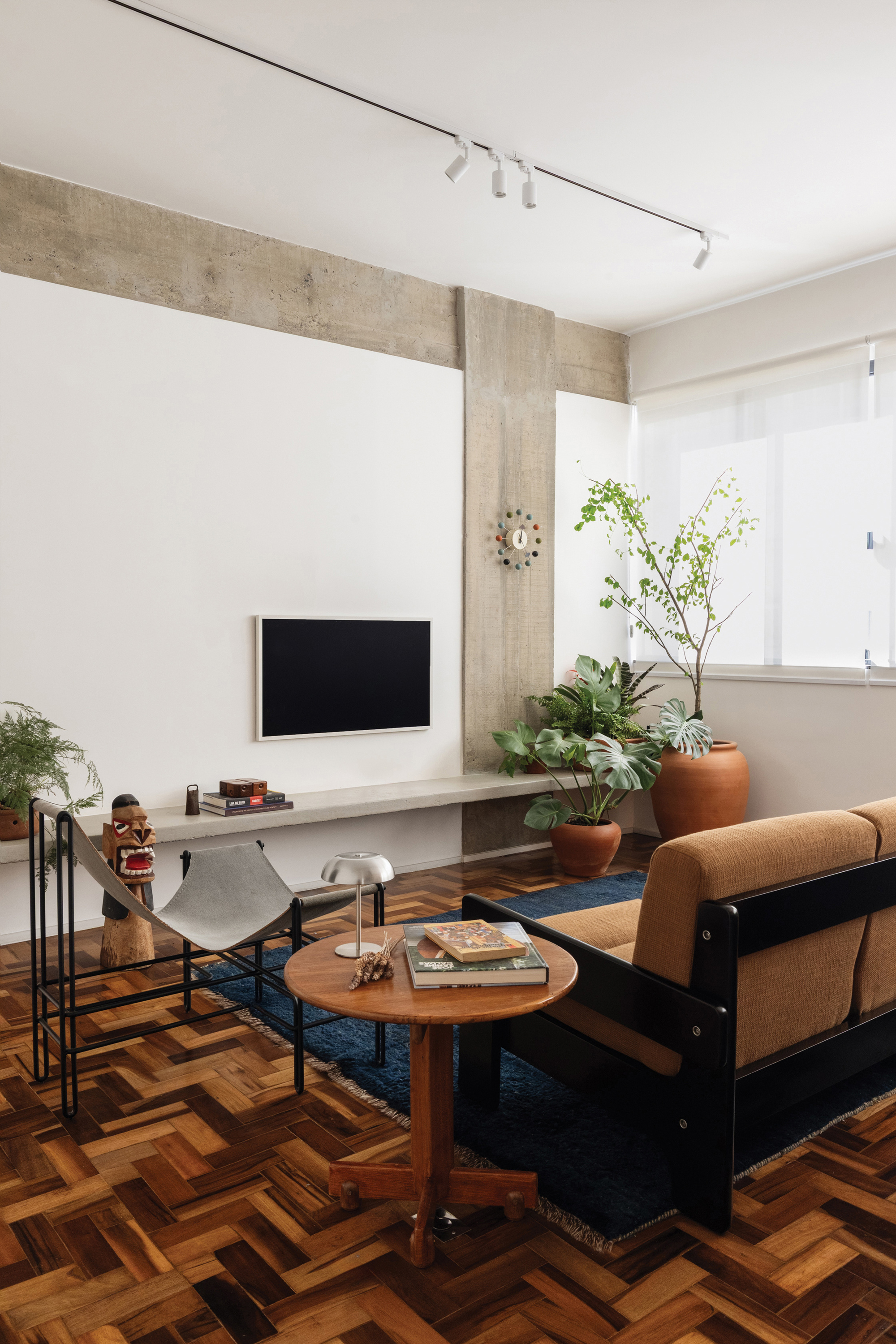Low concrete shelf under a wall-mounted screen, with a round timber side table and leather sling chair on parquet in afternoon light
