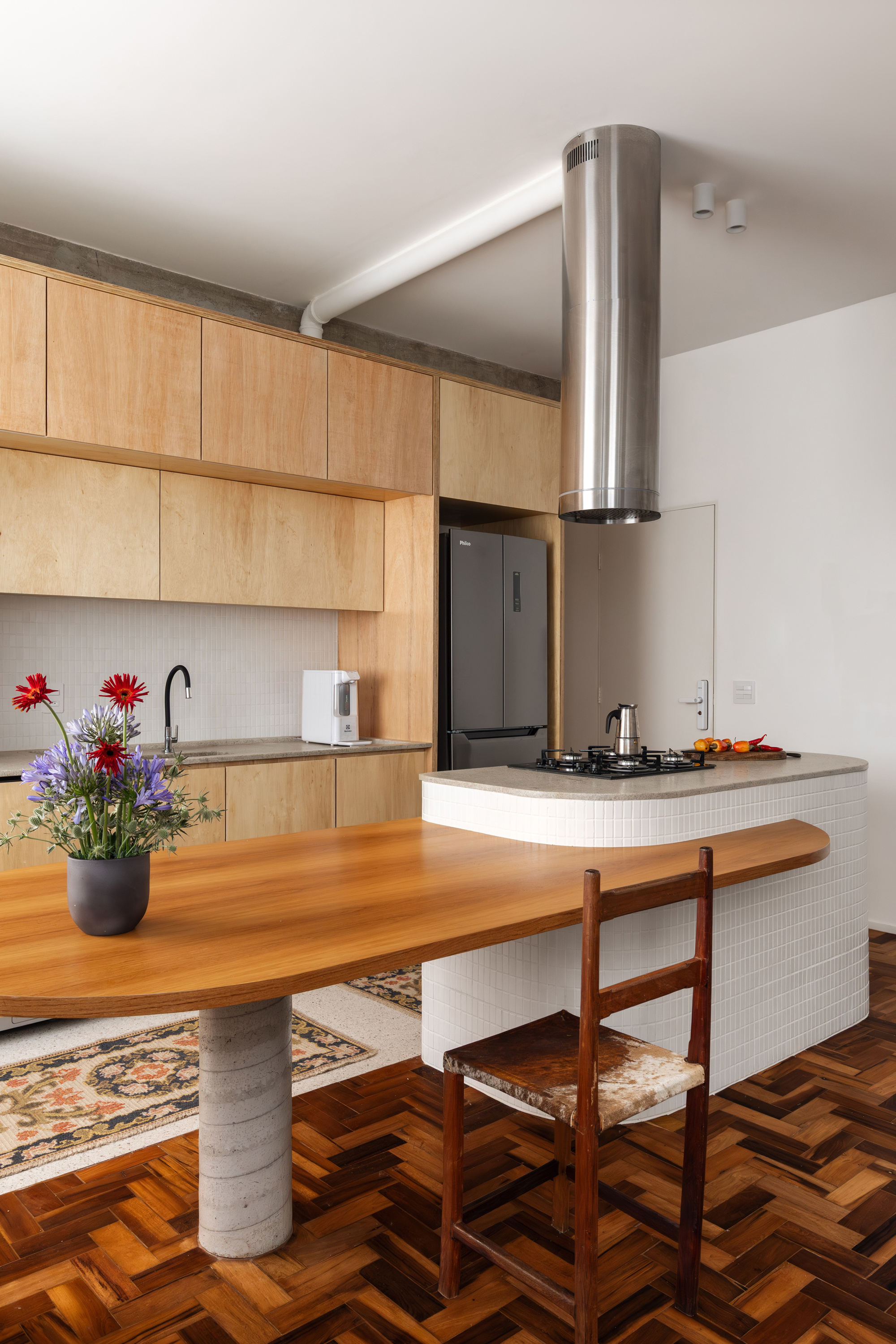 Tiled curved kitchen island beside a round steel extractor hood, with the oak table and parquet floor in the foreground