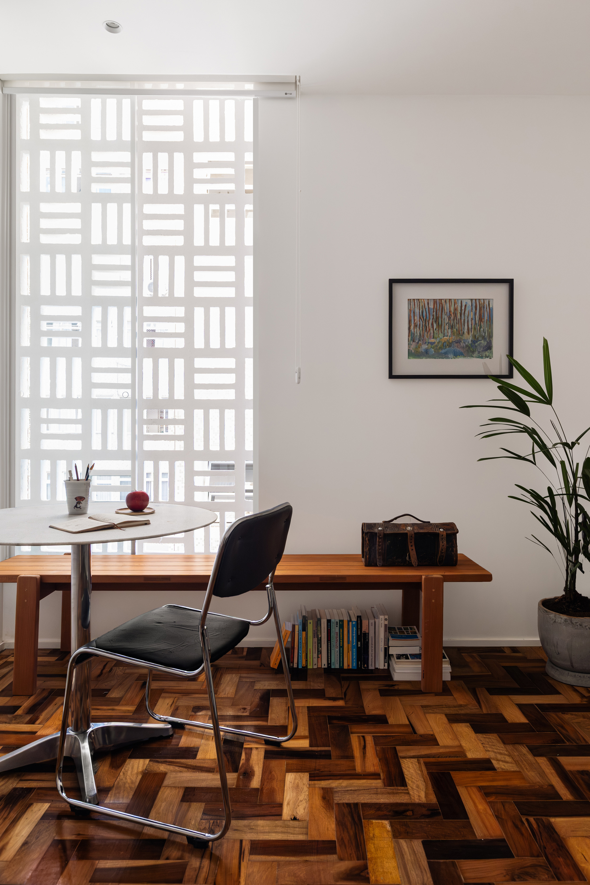 Perforated white screen over a tall window, with a round table, wooden bench and bookshelf in soft daylight on parquet