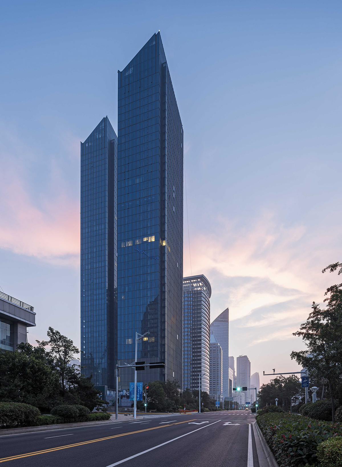 Two blue glass towers with angled tops beside an empty road at dusk, pink clouds in the sky