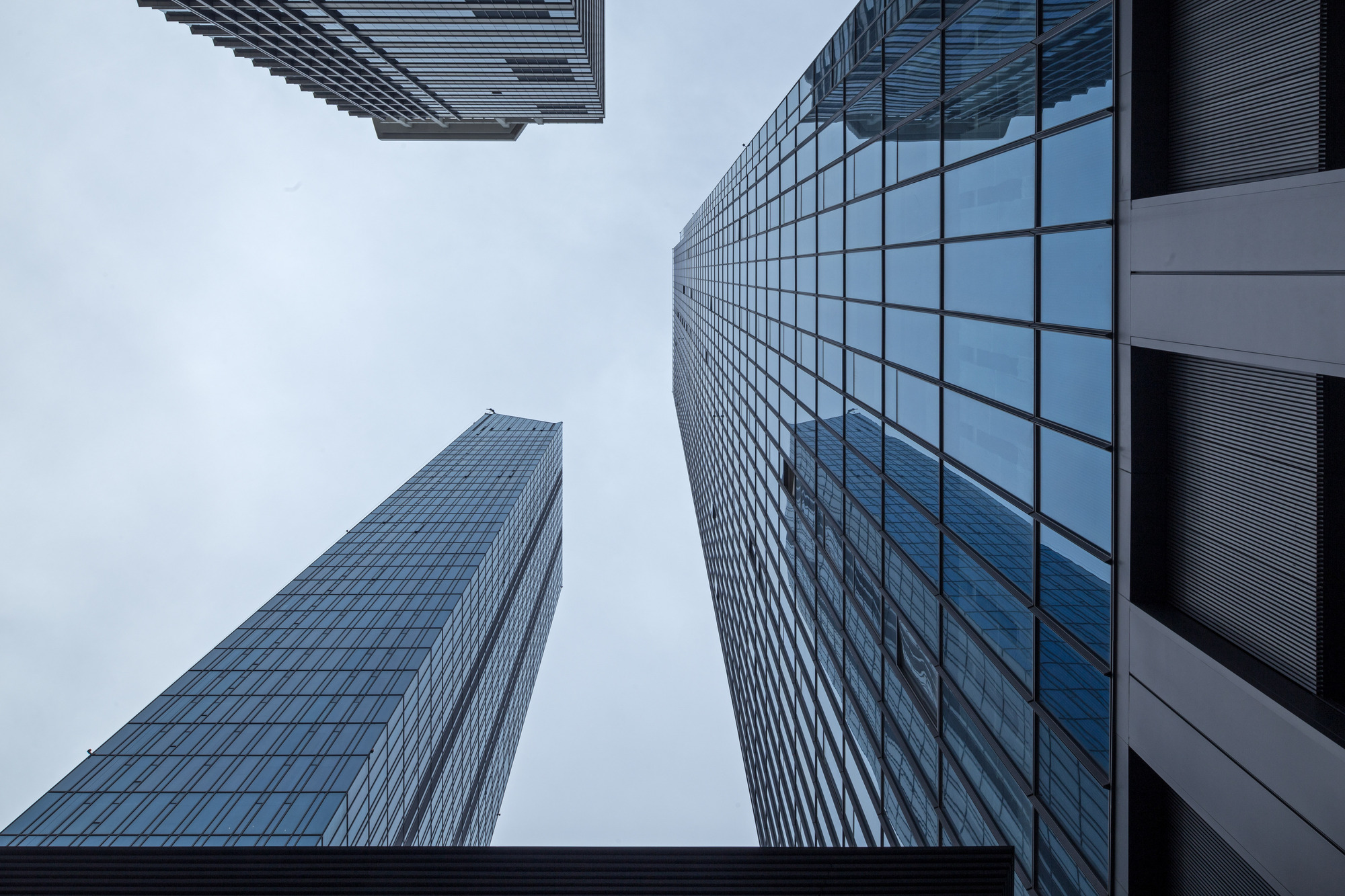Upward view of glass curtain wall towers converging against an overcast grey sky