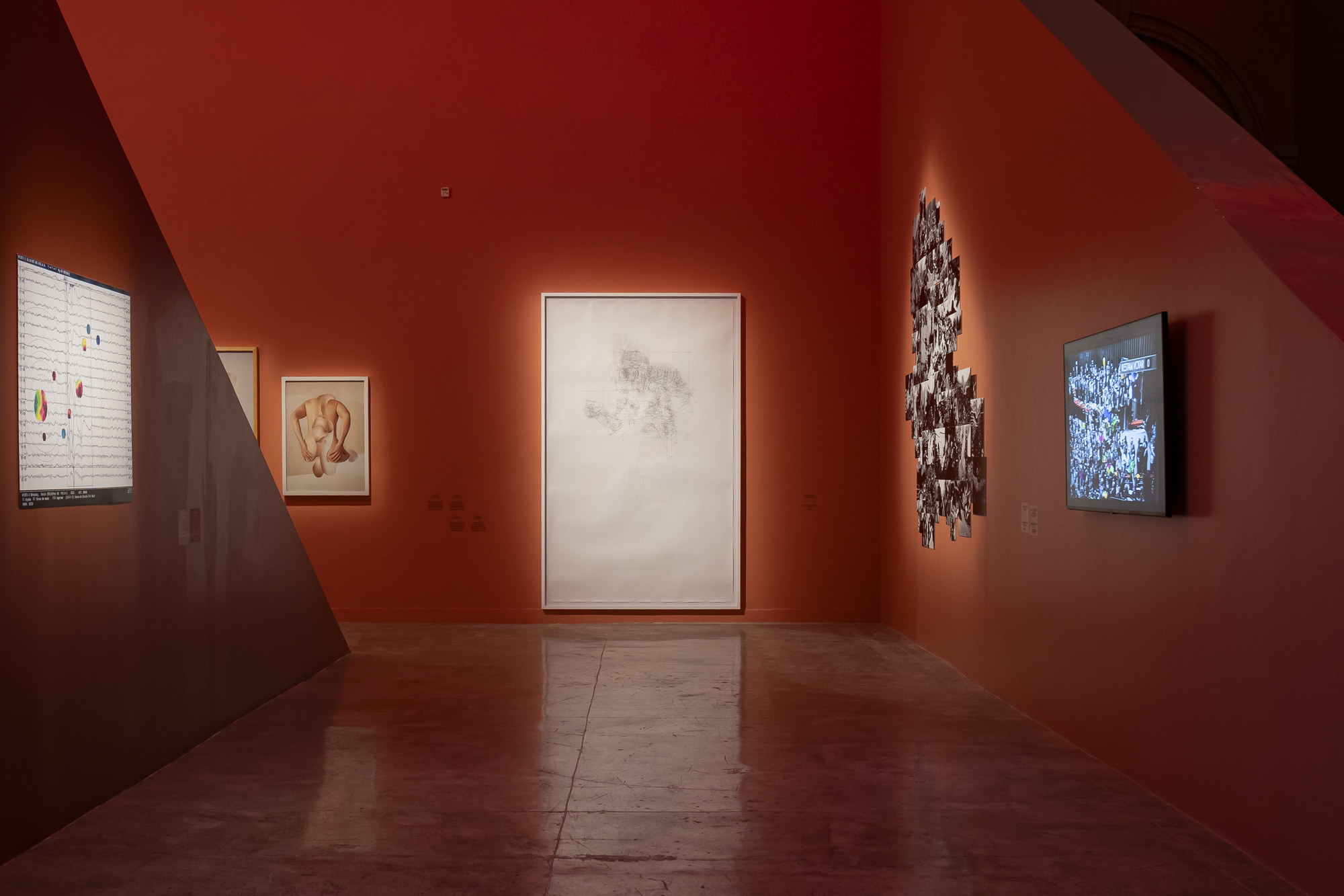 Orange gallery corridor with a large pale drawing at center, a photo collage and a video screen glowing along the walls