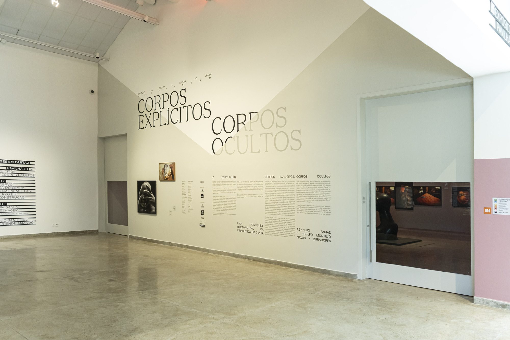 Entrance wall with large black and grey lettering and a text panel, and an open doorway revealing the lit gallery beyond