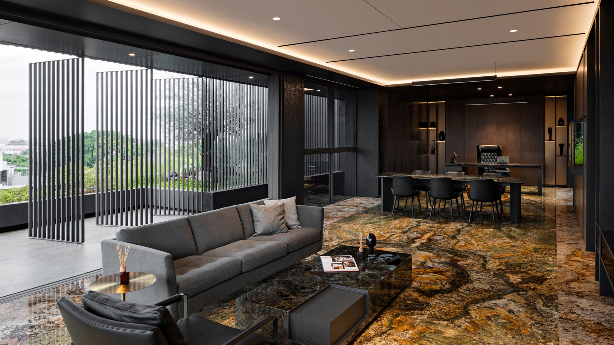 Executive lounge with grey sofa and veined stone floor, sliding black fin screens opening onto a terrace with treetops under overcast daylight