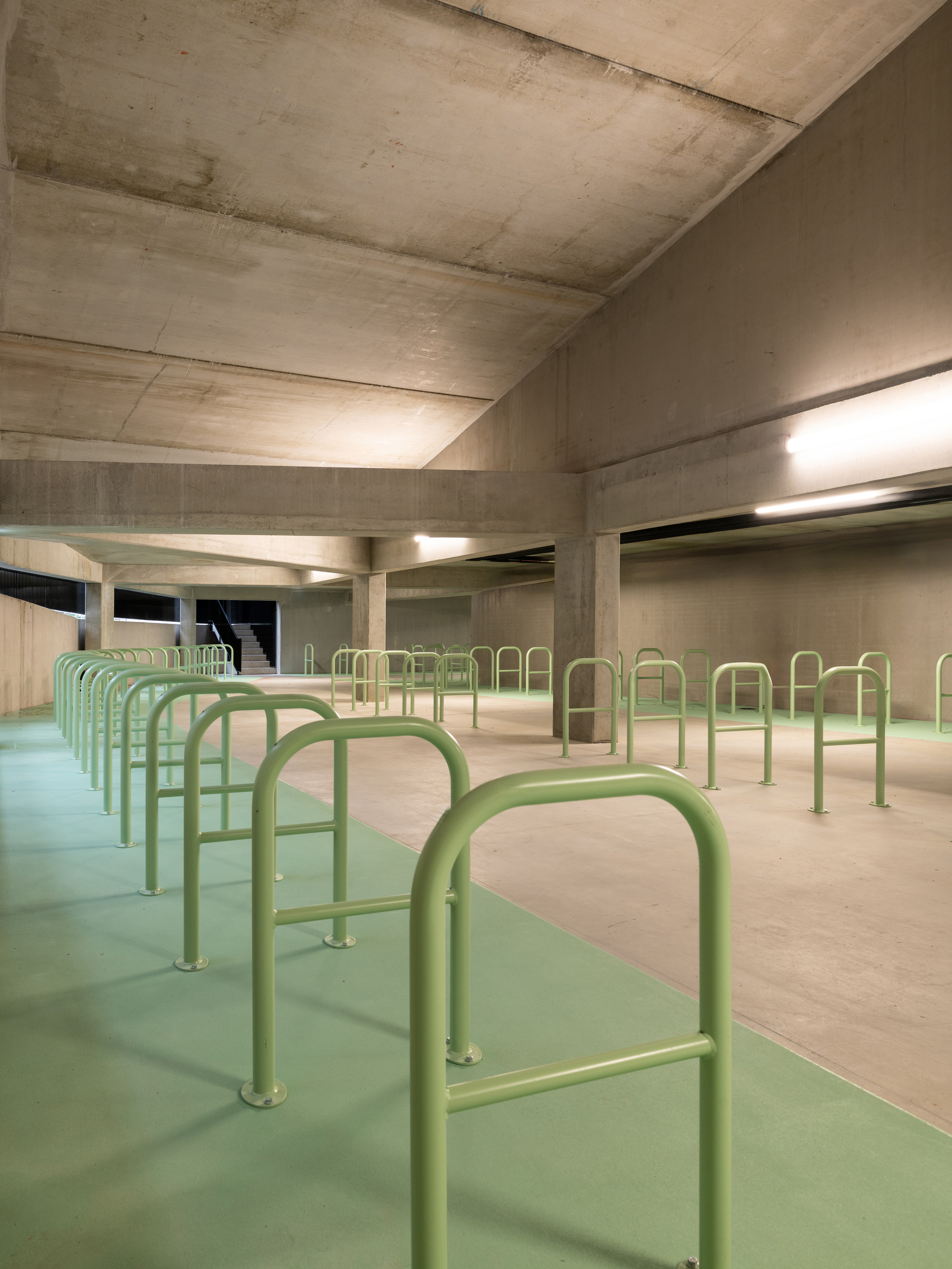 Covered bicycle parking floor with green steel hoops on a green painted lane beneath a raw concrete ceiling and beams