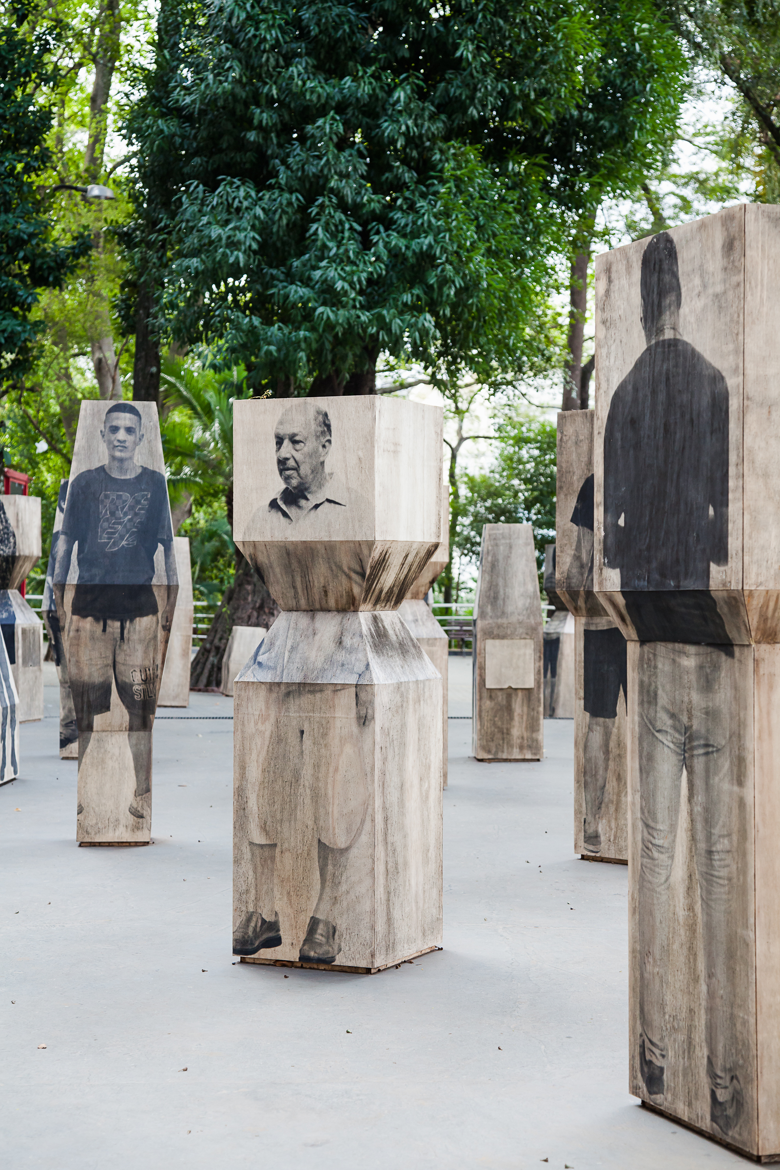 Close view of timber blocks printed with portraits of men, standing among trees on a grey paved court
