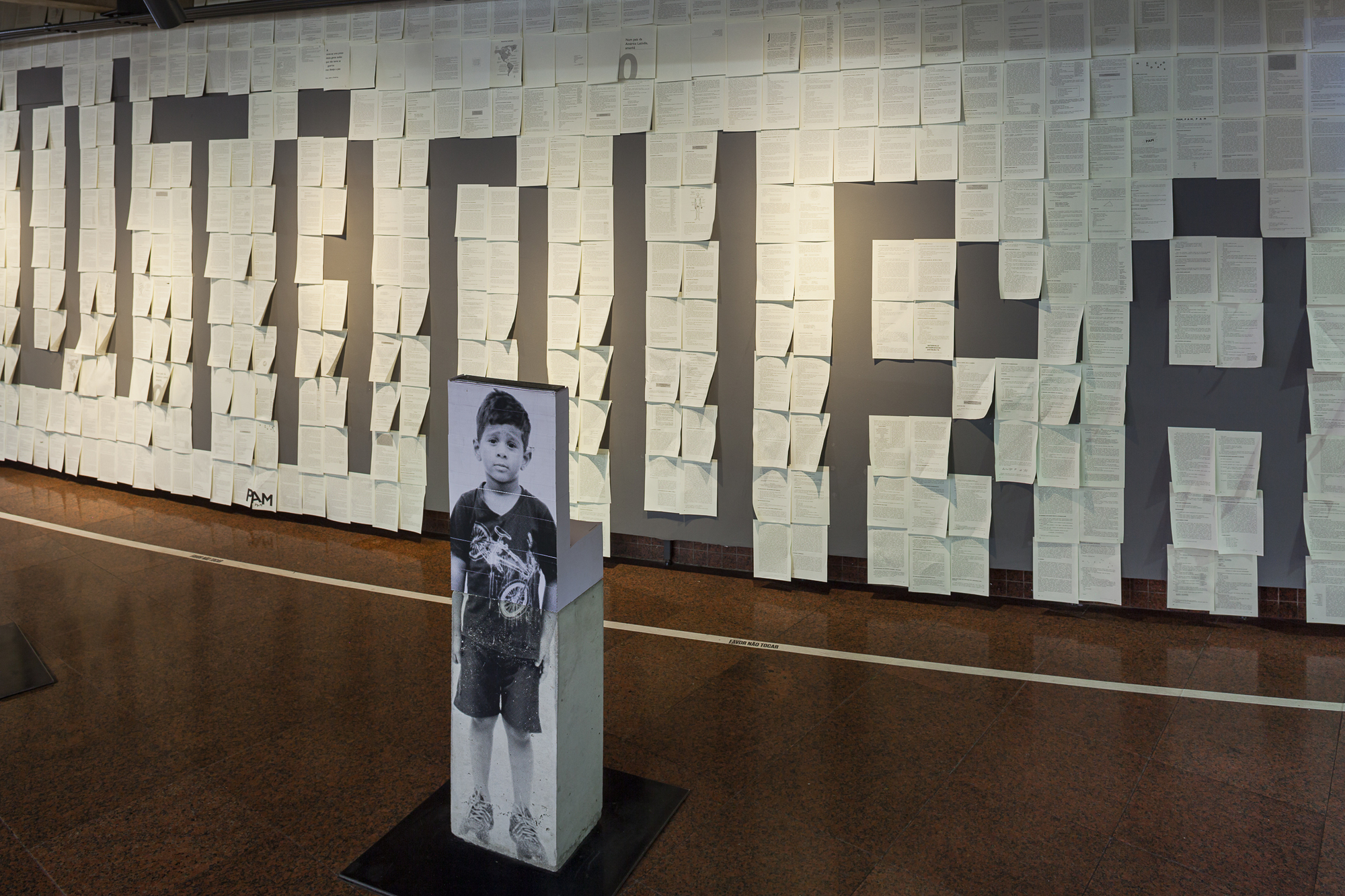 Printed sheets of paper pasted on a grey wall forming large letters, beside a column printed with a boy's portrait